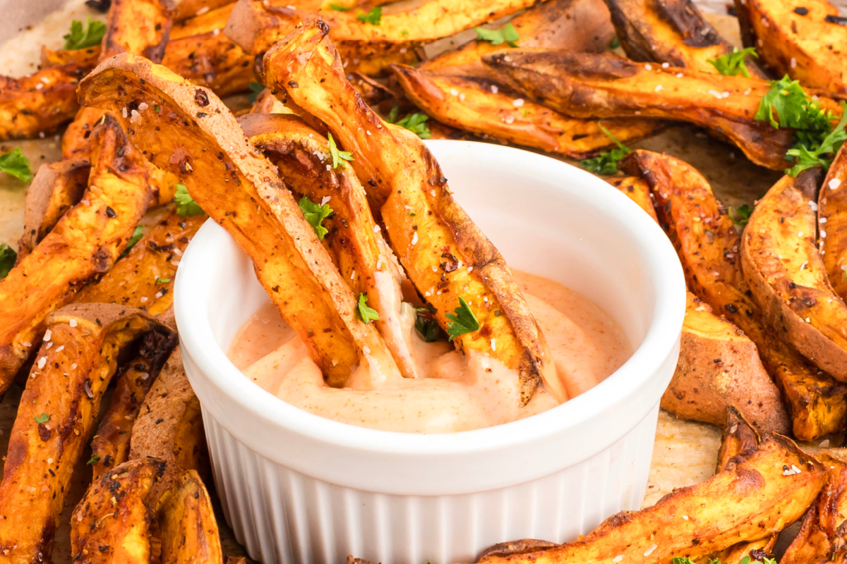 Oven-baked sweet potato fries being dipped into sauce.