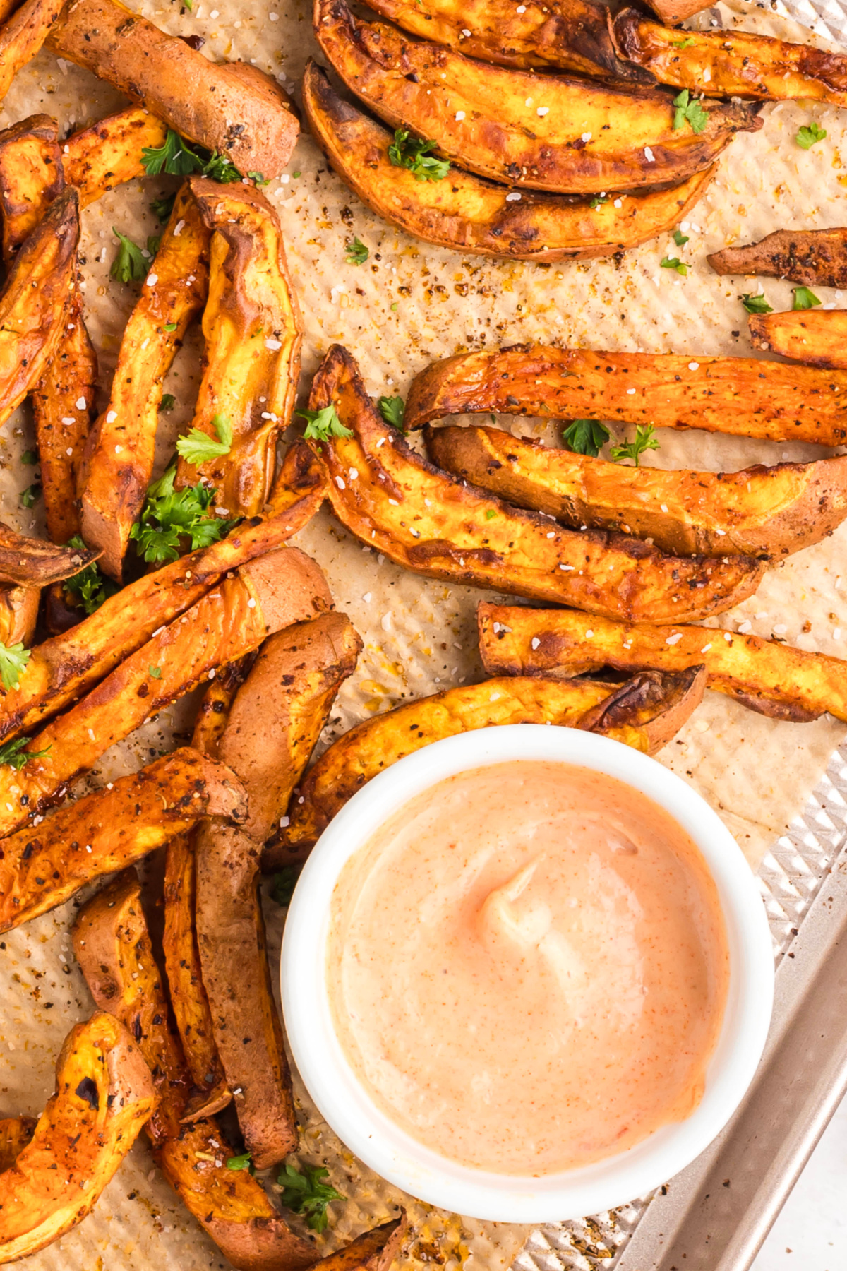 Dipping sauce in the middle of a sheet pan with sweet potato fries.