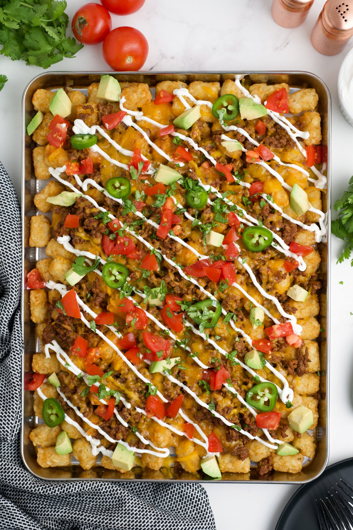 Tomato, avocado, sour cream, jalapeño, and cilantro added to the top to finish these tater tot nachos.