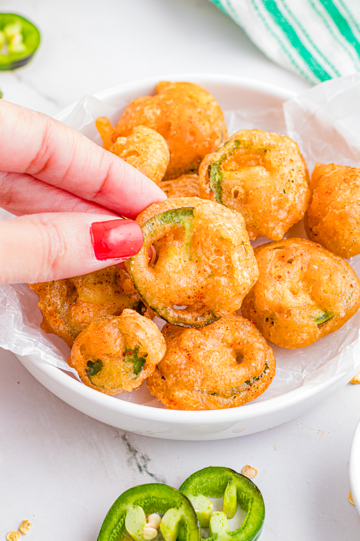 A plate with fried beer battered jalapenos and one being held up.