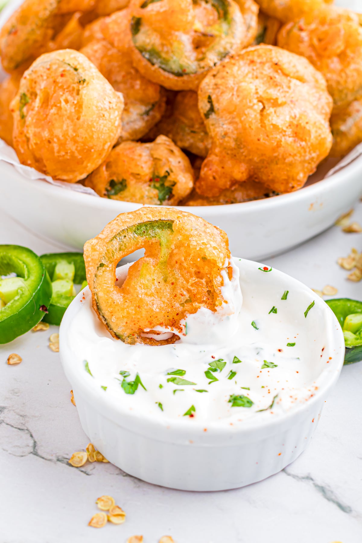 A battered jalapeno being dipped in a sauce.