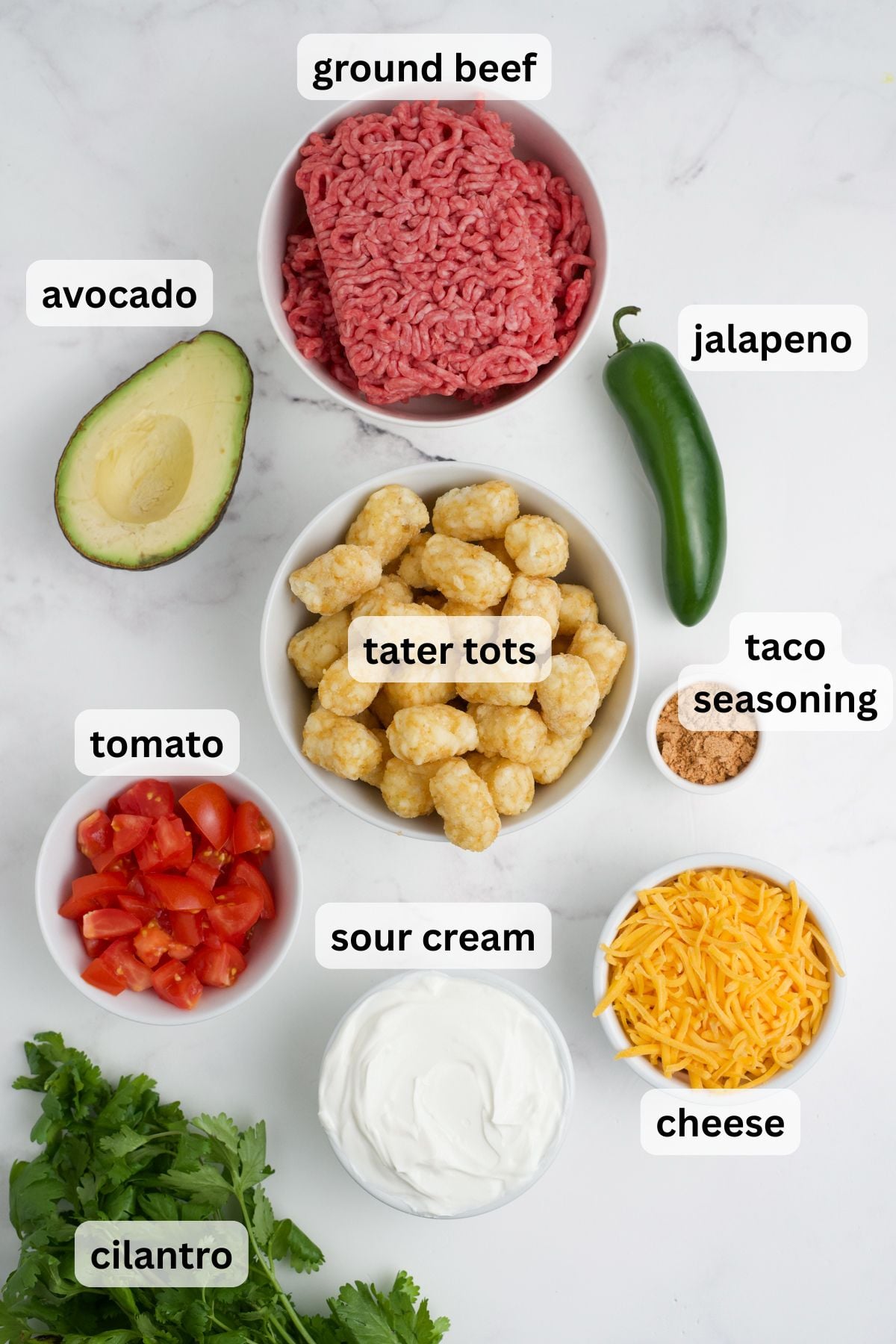 Ingredients to make nachos with tater tots in bowls on a table.