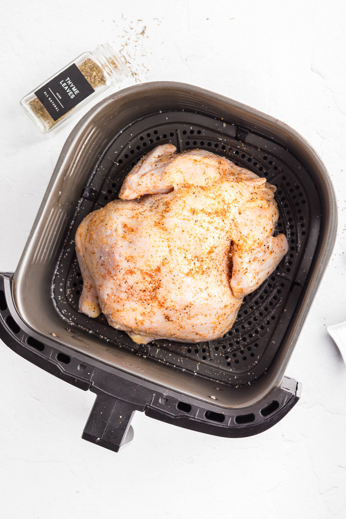 A chicken seasoned into the air fryer to cook.