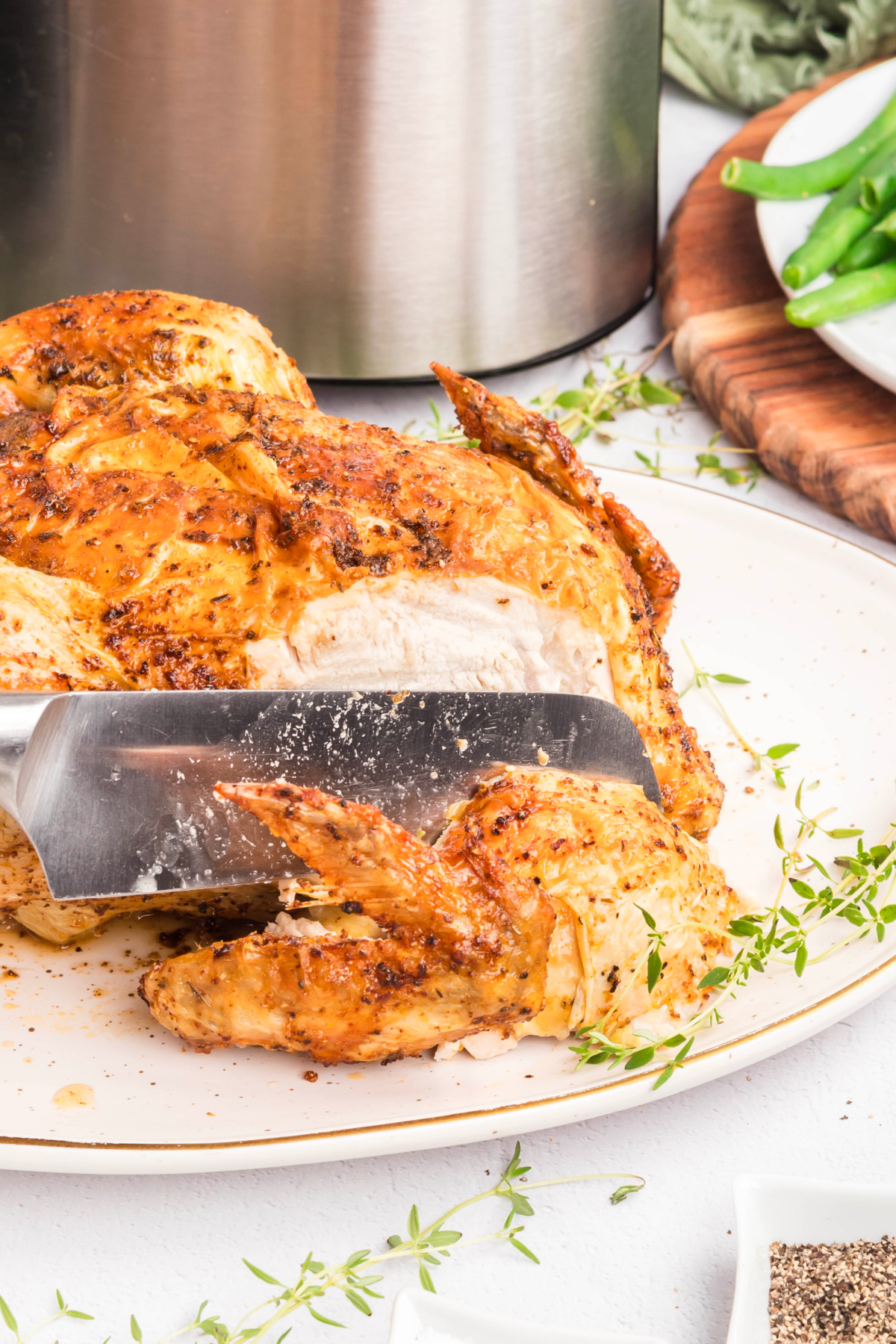 A knife cutting the wing of a whole chicken.