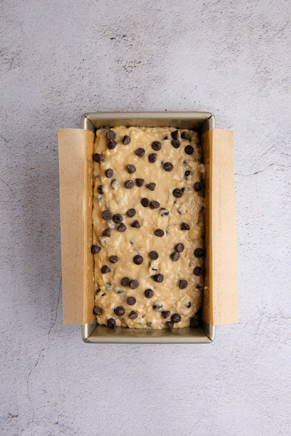 Chocolate chip batter in a parchment covered loaf pan on the counter.
