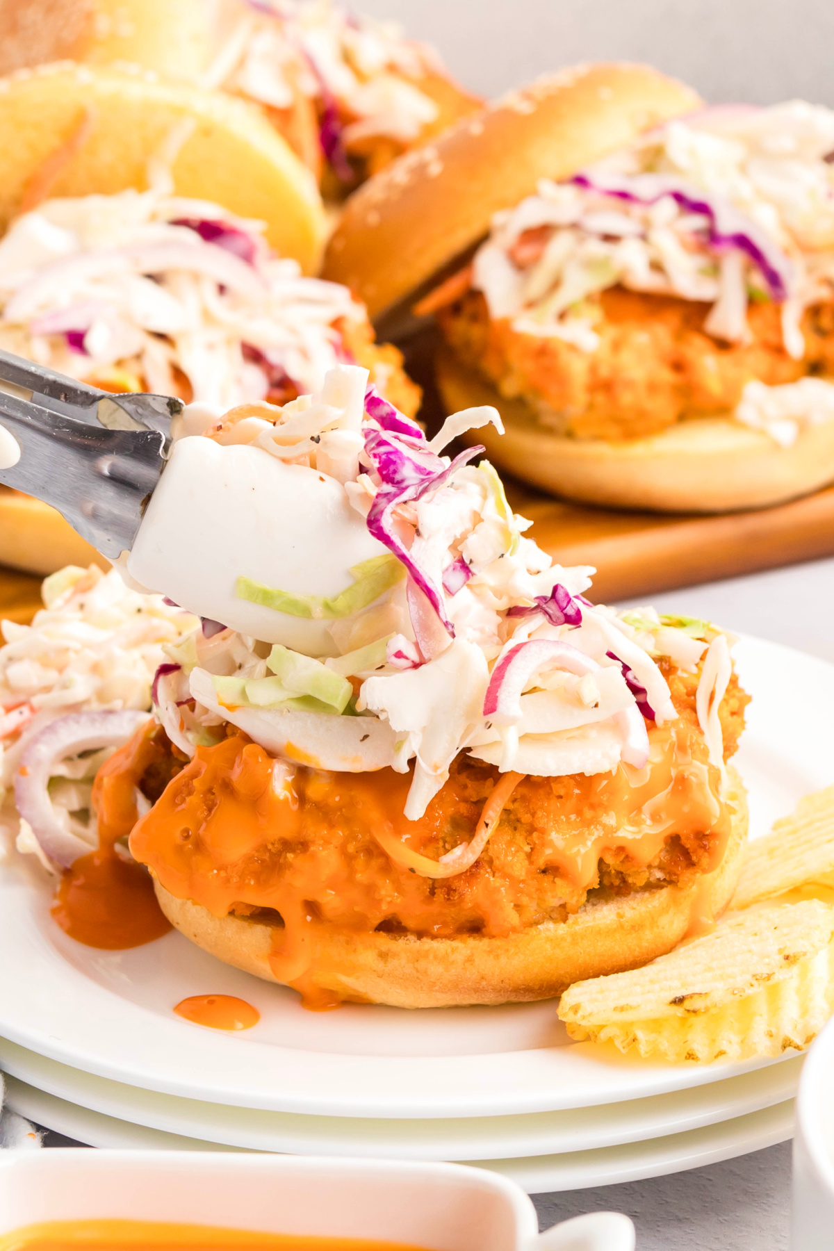 A buffalo chicken sandwich with colesalaw being put on top.