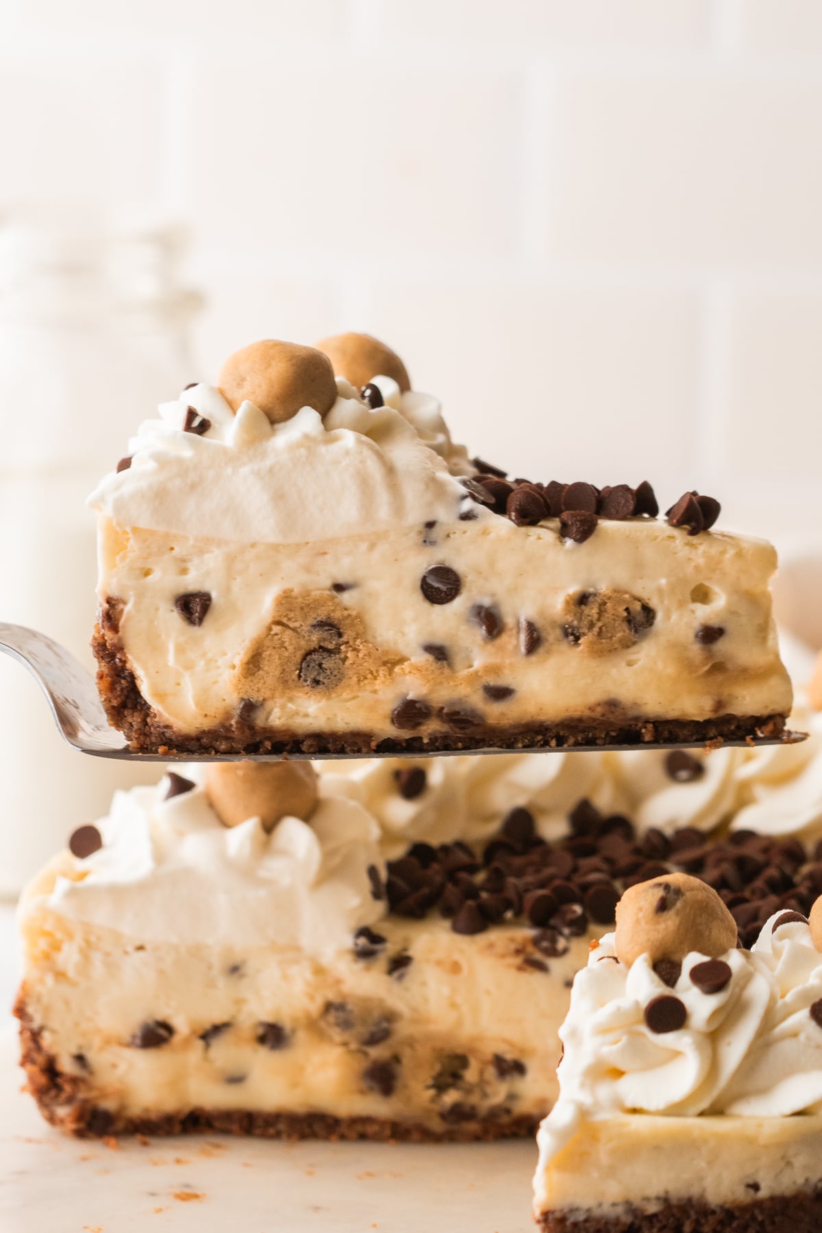 A slice of cheesecake with cookie dough and chocolate chips being held up in the air.