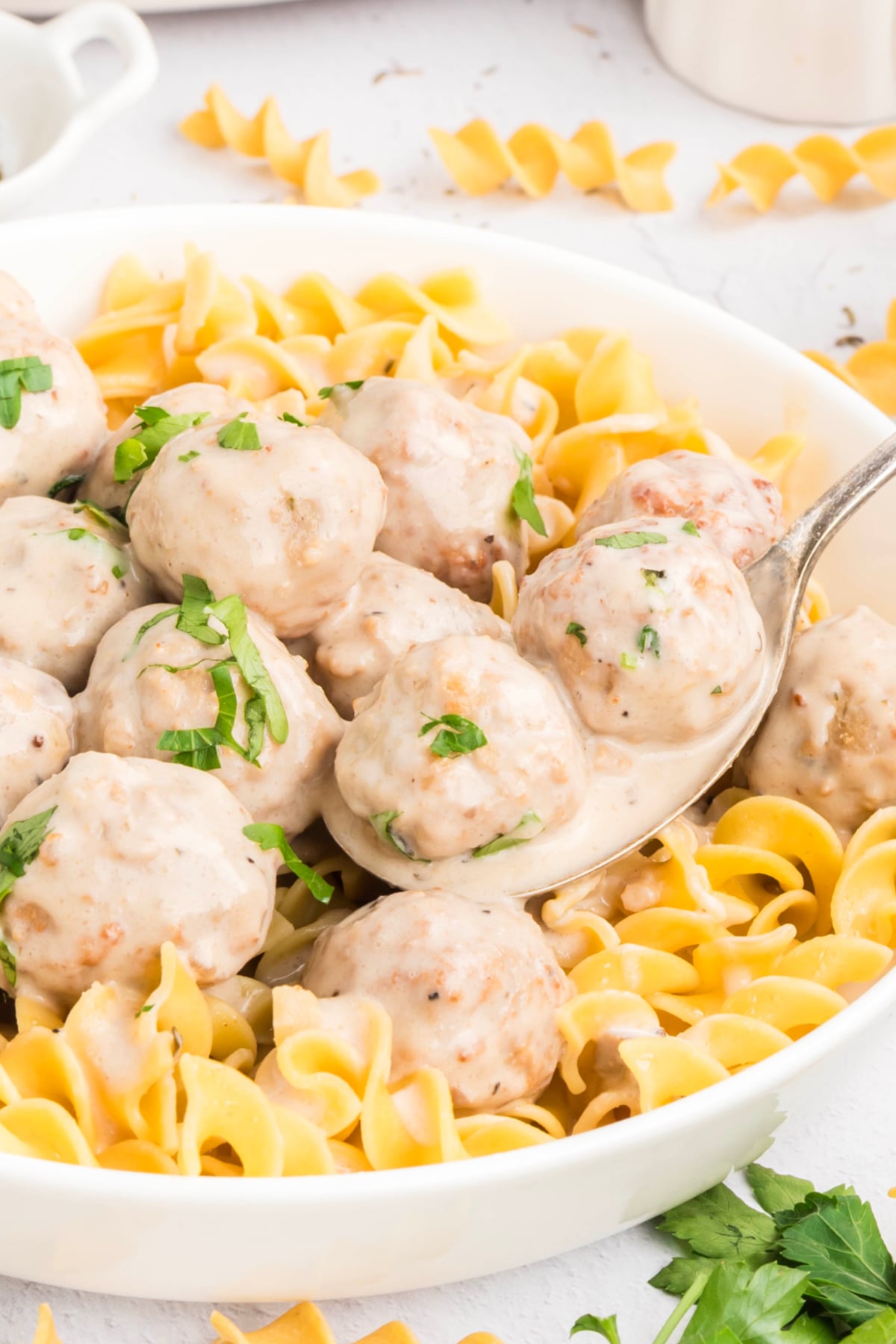 A spoon holding Swedish meatballs in sauce over egg noodles. 