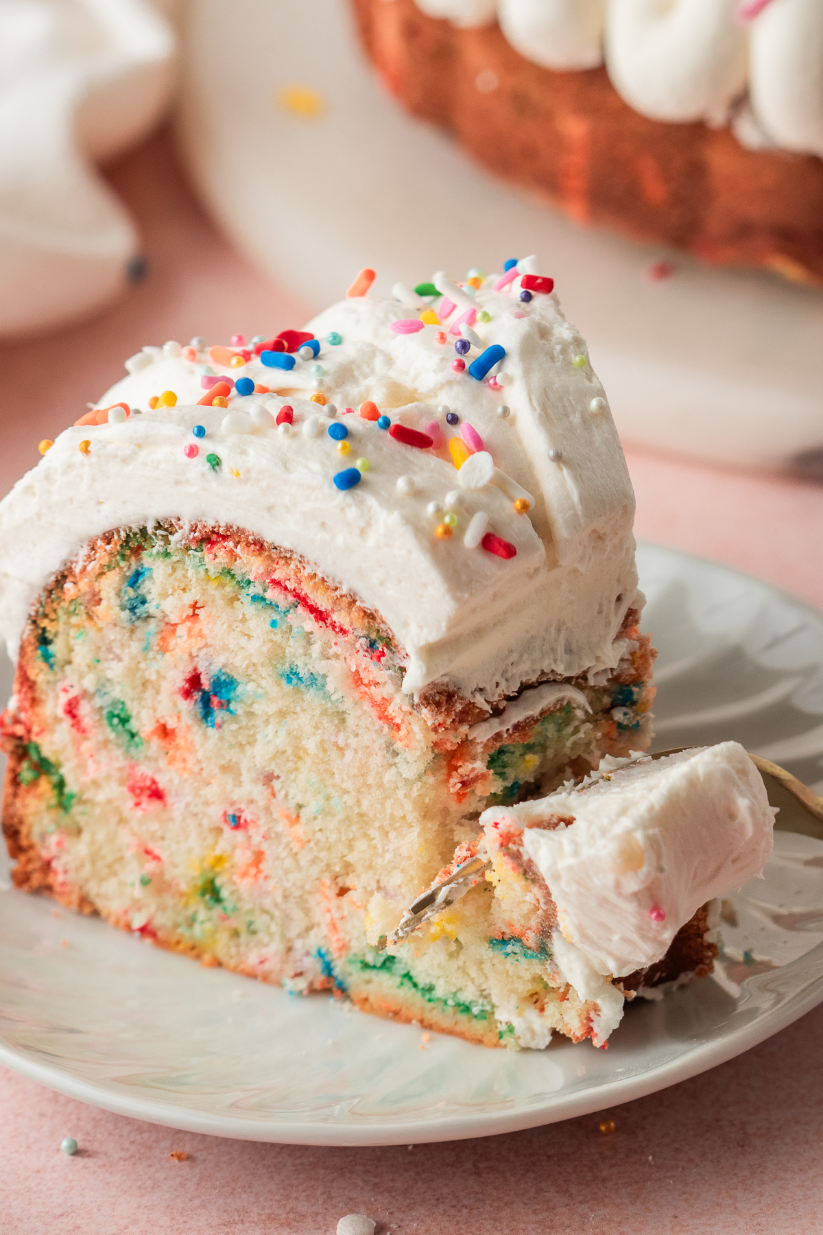 A fork taking a piece of sprinkles bundt cake off a plate.