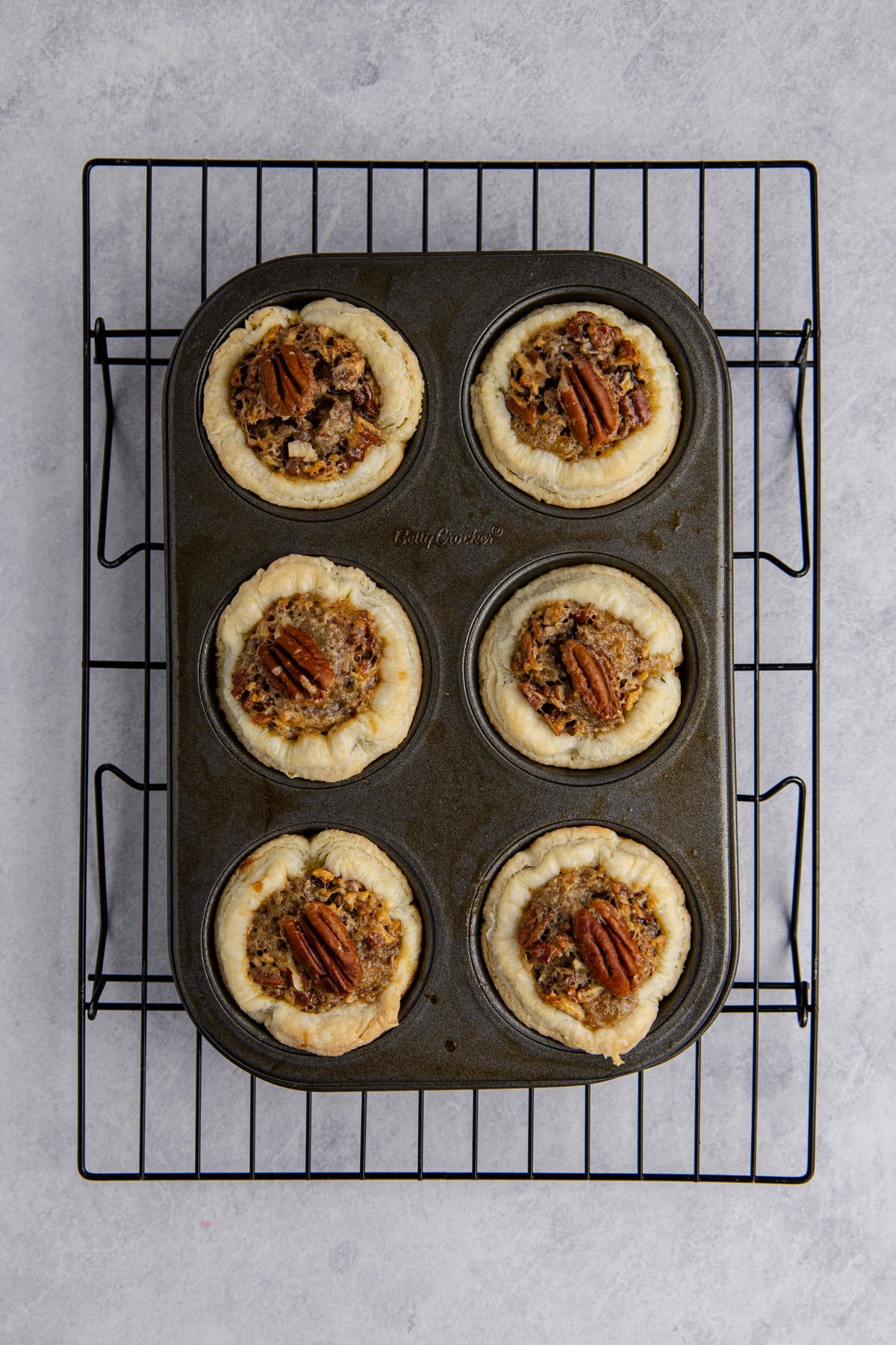Baked mini pecan pies on rack.