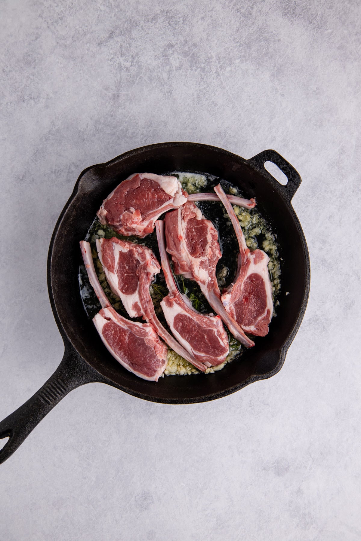 Butter, thyme, salt, and garlic in a cast iron skillet with lamb chops added.