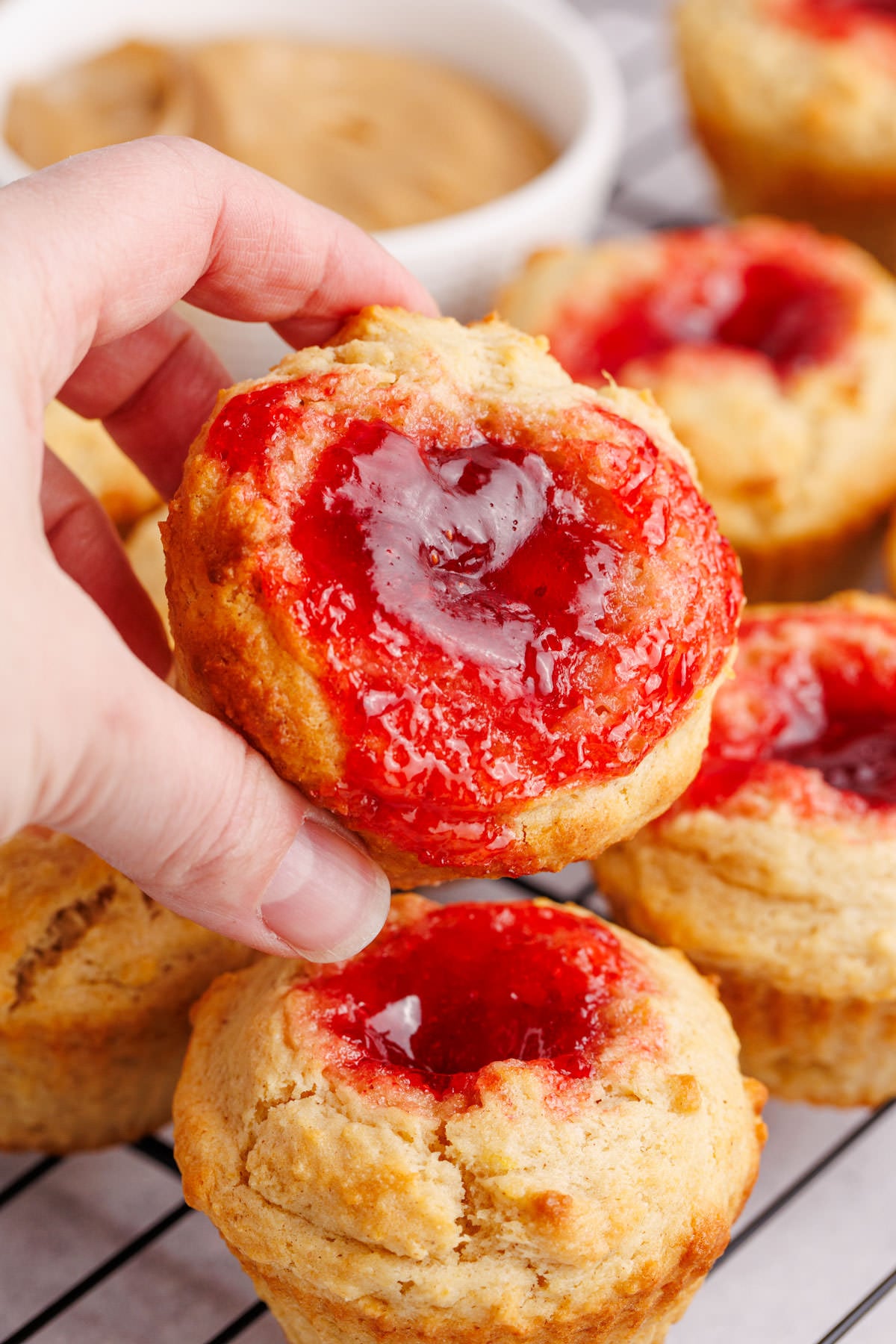 A hand holding up a muffin with peanut butter and jelly.