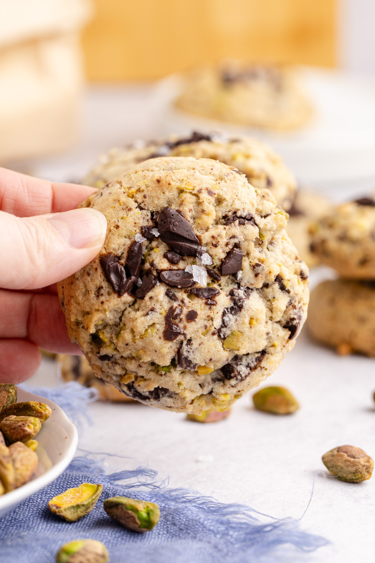 A cookie with chocolate chips and pistachios being held up in the air.