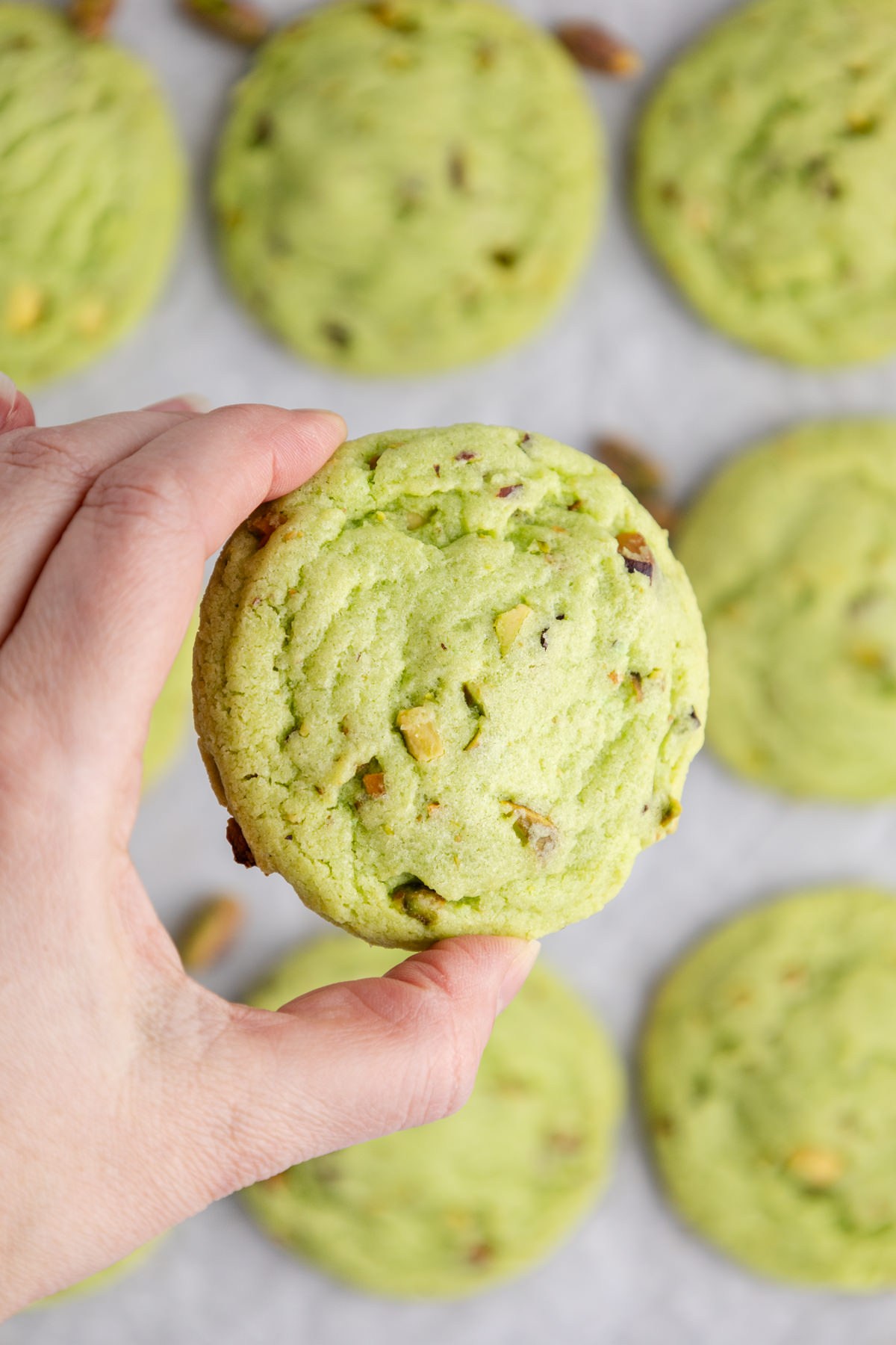 A cookie with pistachio pieces held up in the air.