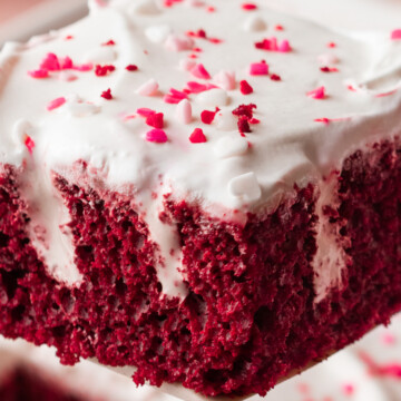 A slice of red velvet poke cake being held up in the air.