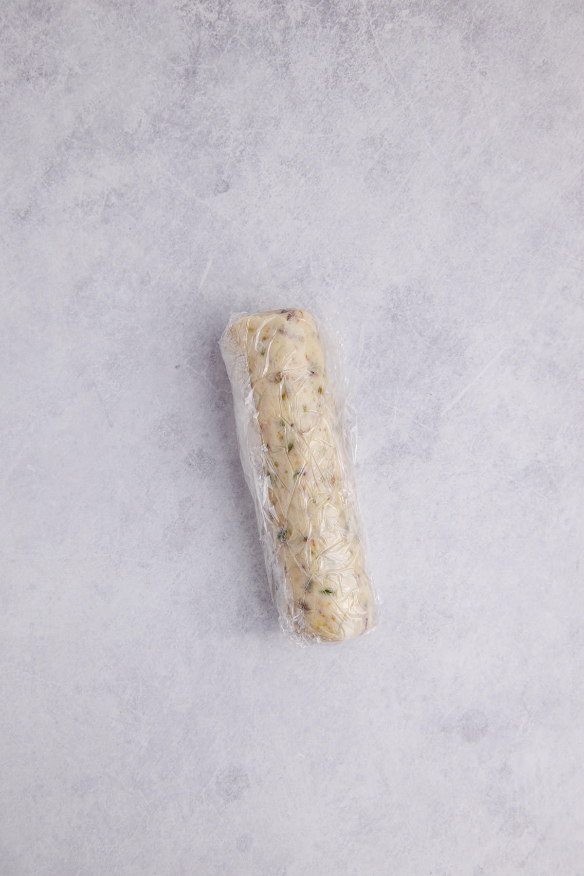 Dough ball formed into a log and covered with plastic wrap.