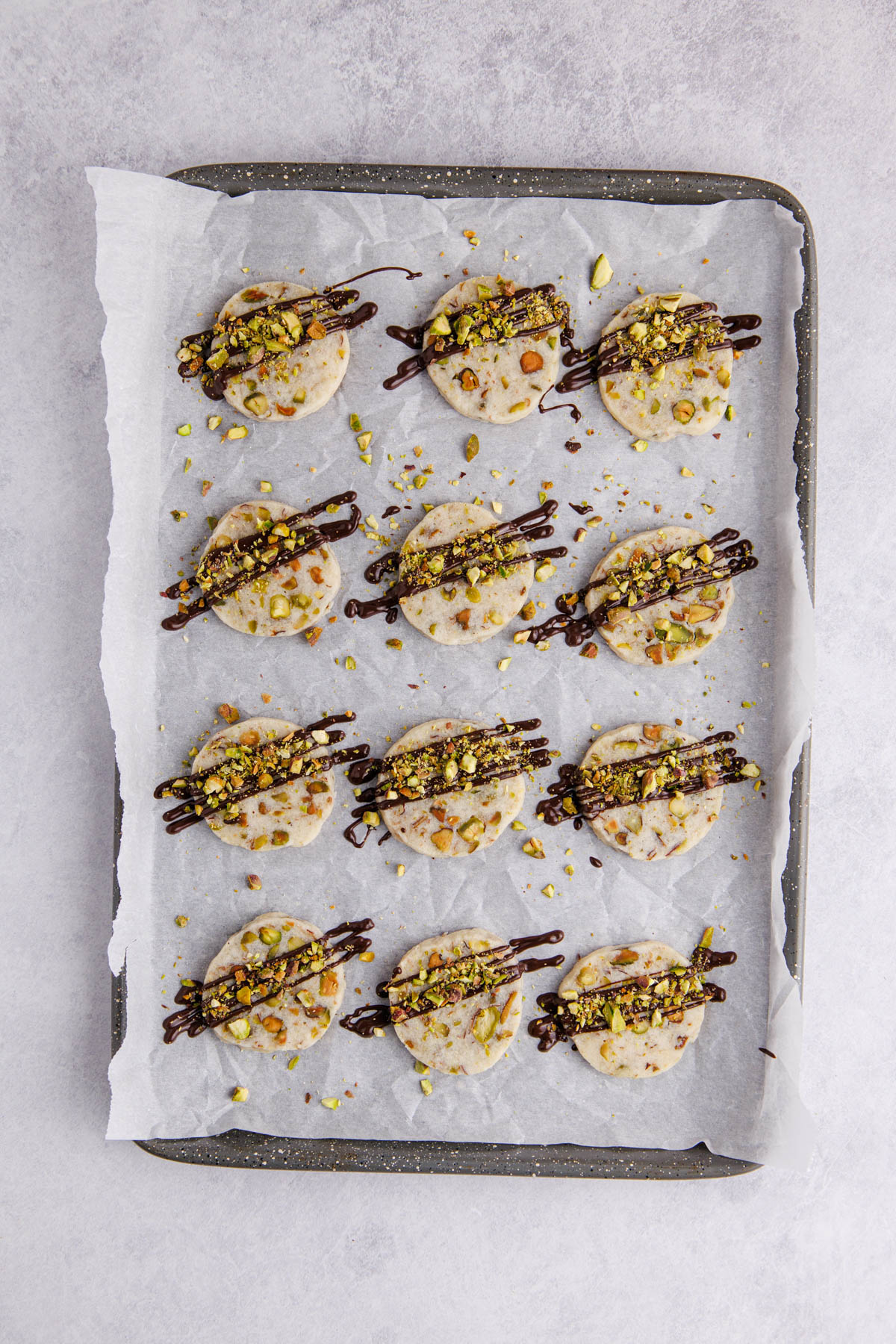 Cookies cooling and melted chocolate and crushed pistachios drizzled on top.
