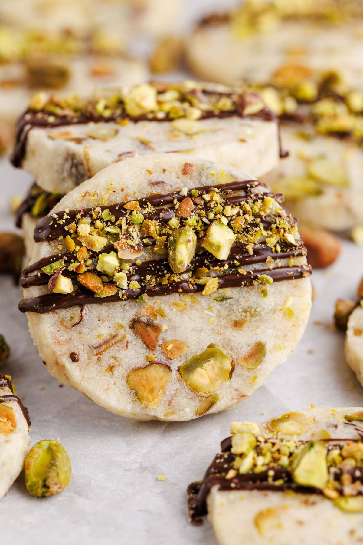 Cookies with chocolate and pistachios stacked on top of one another with one leaning in front.