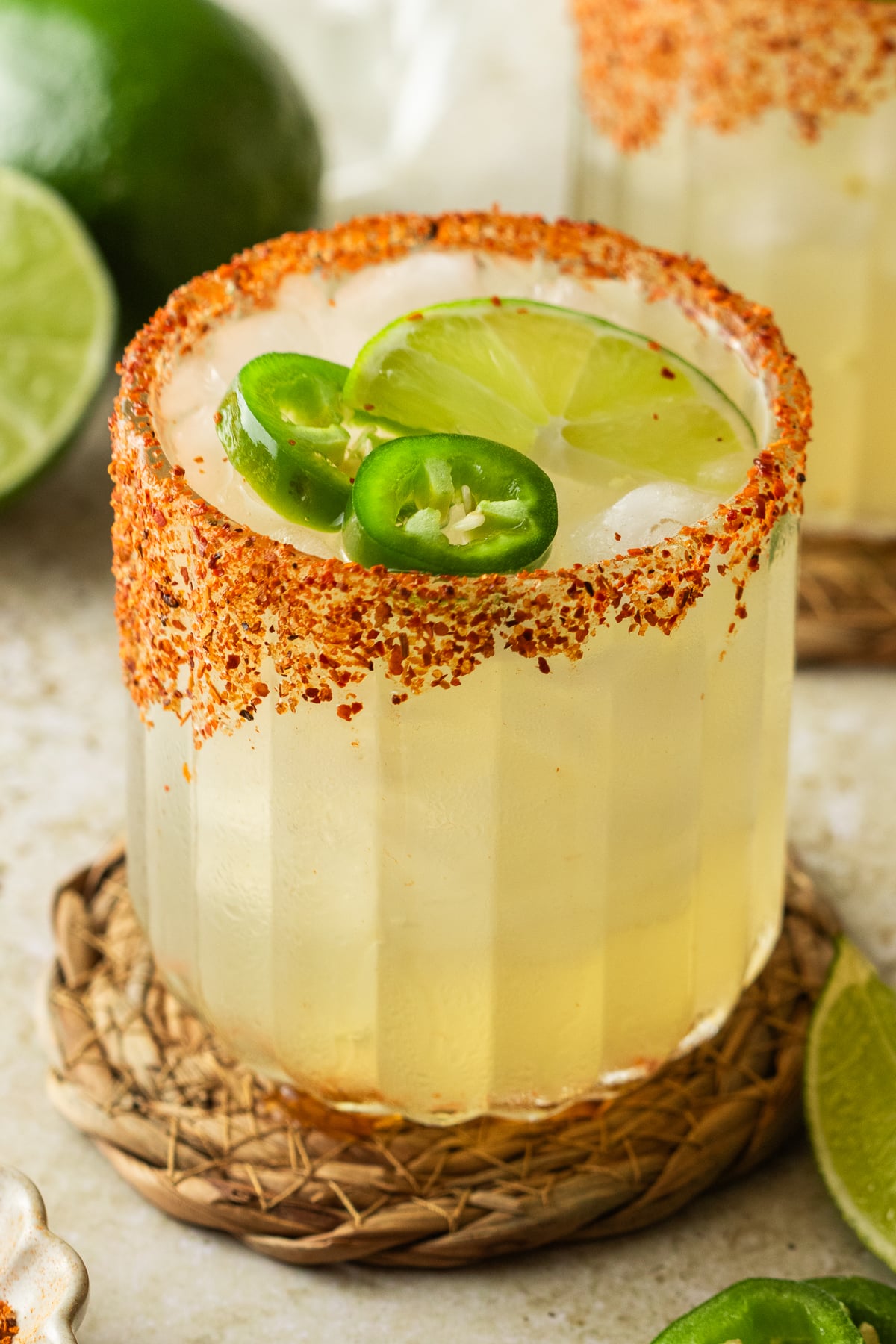 Margaritas in a glass on a table garnished with jalapeno and lime.