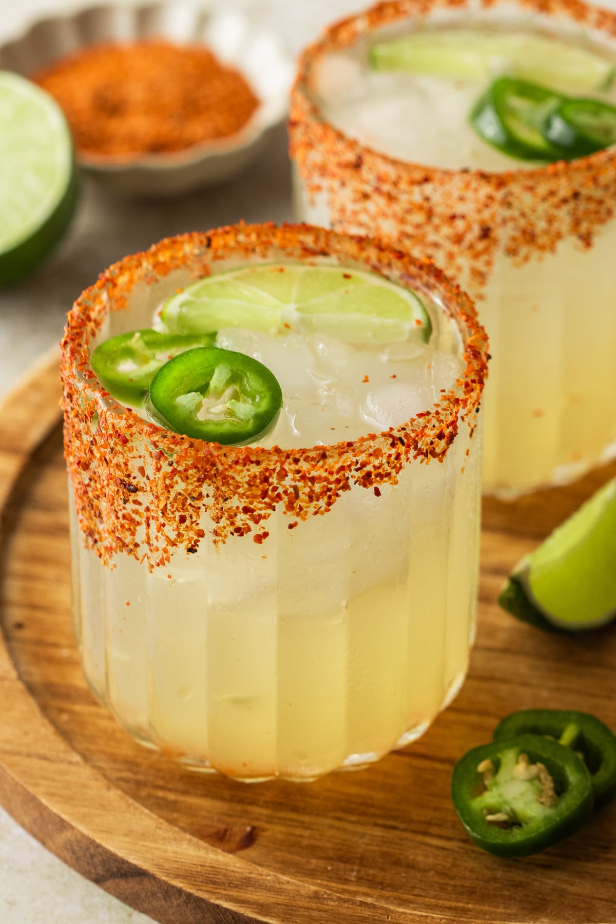 Margaritas in a glass on a table garnished with jalapeno and lime.