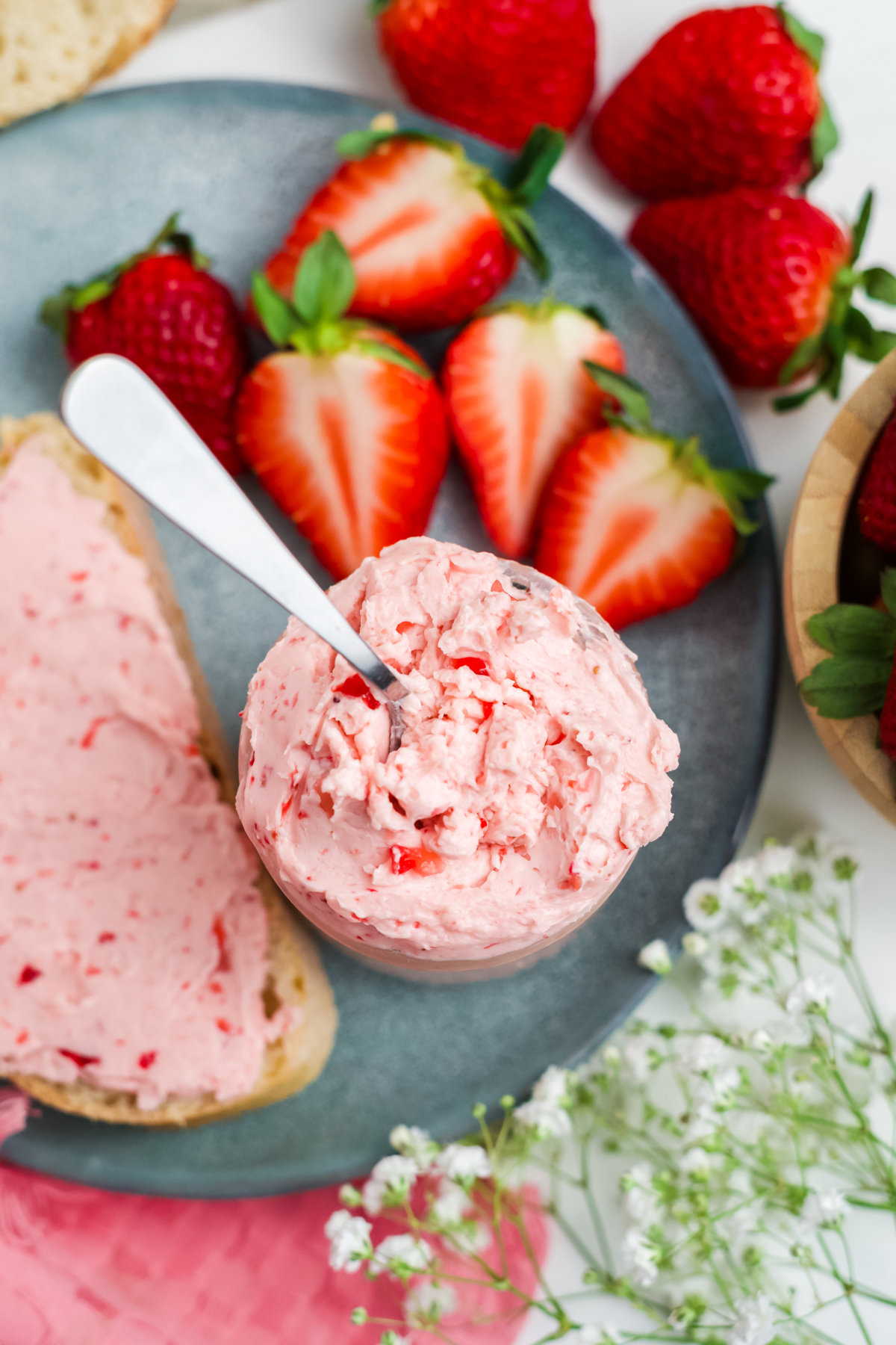 A plate with a jar full of butter with a spoon in it, some fresh strawberries and a slice of buttered bread