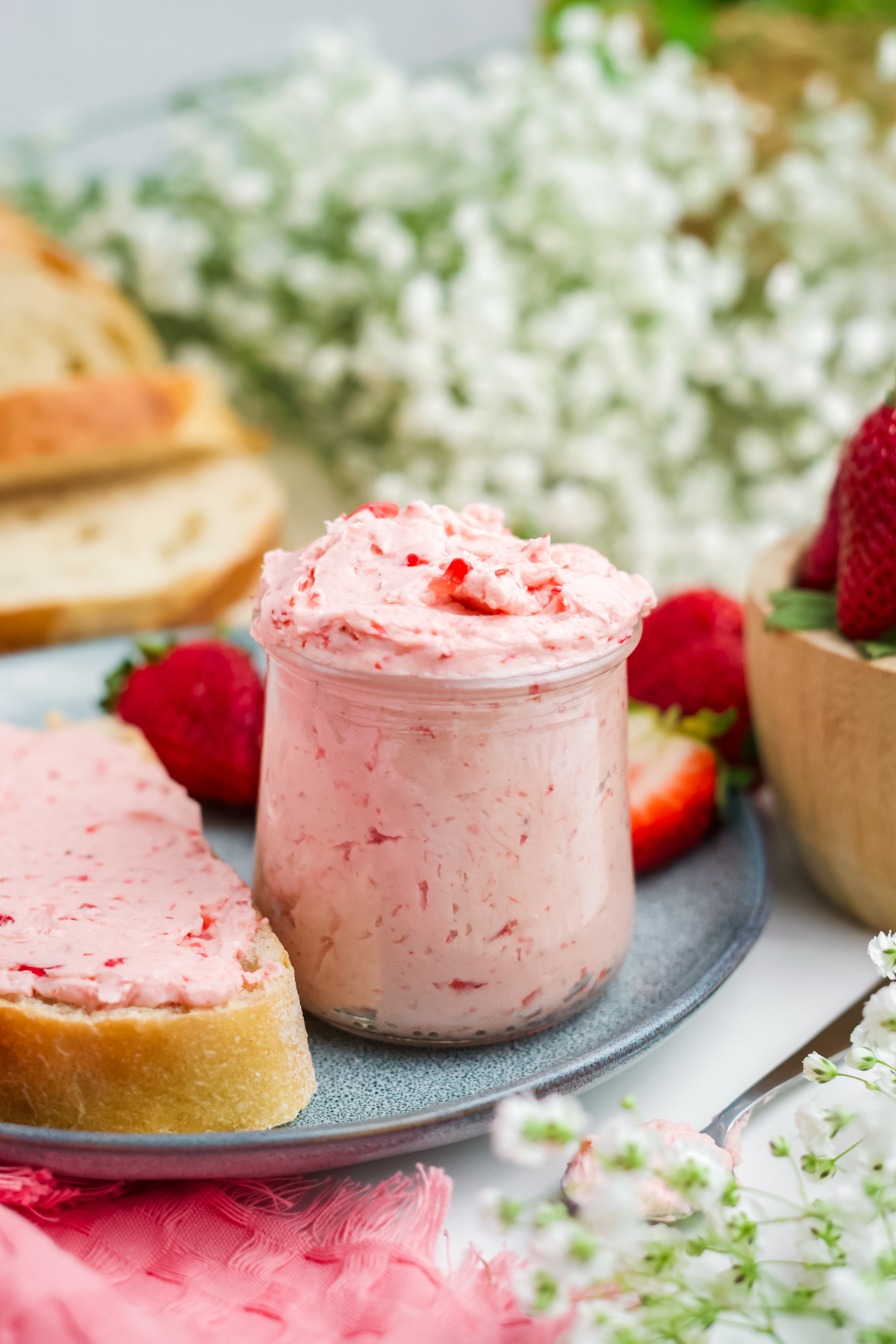 A jar full of butter on plate with buttered bread and strawberries