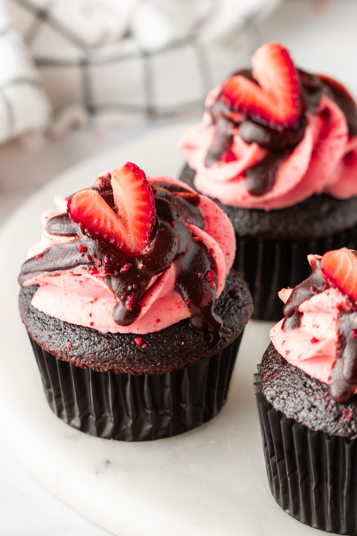 Chocolate cupcakes with strawberry frosting and chocolate ganache on top.