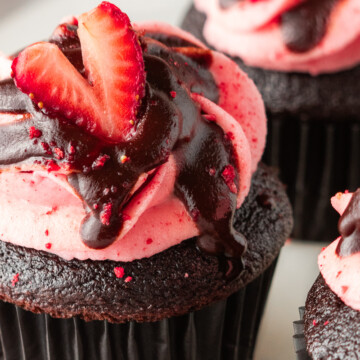 A close up of a chocolate cupcake with icing and a strawberry slice on top