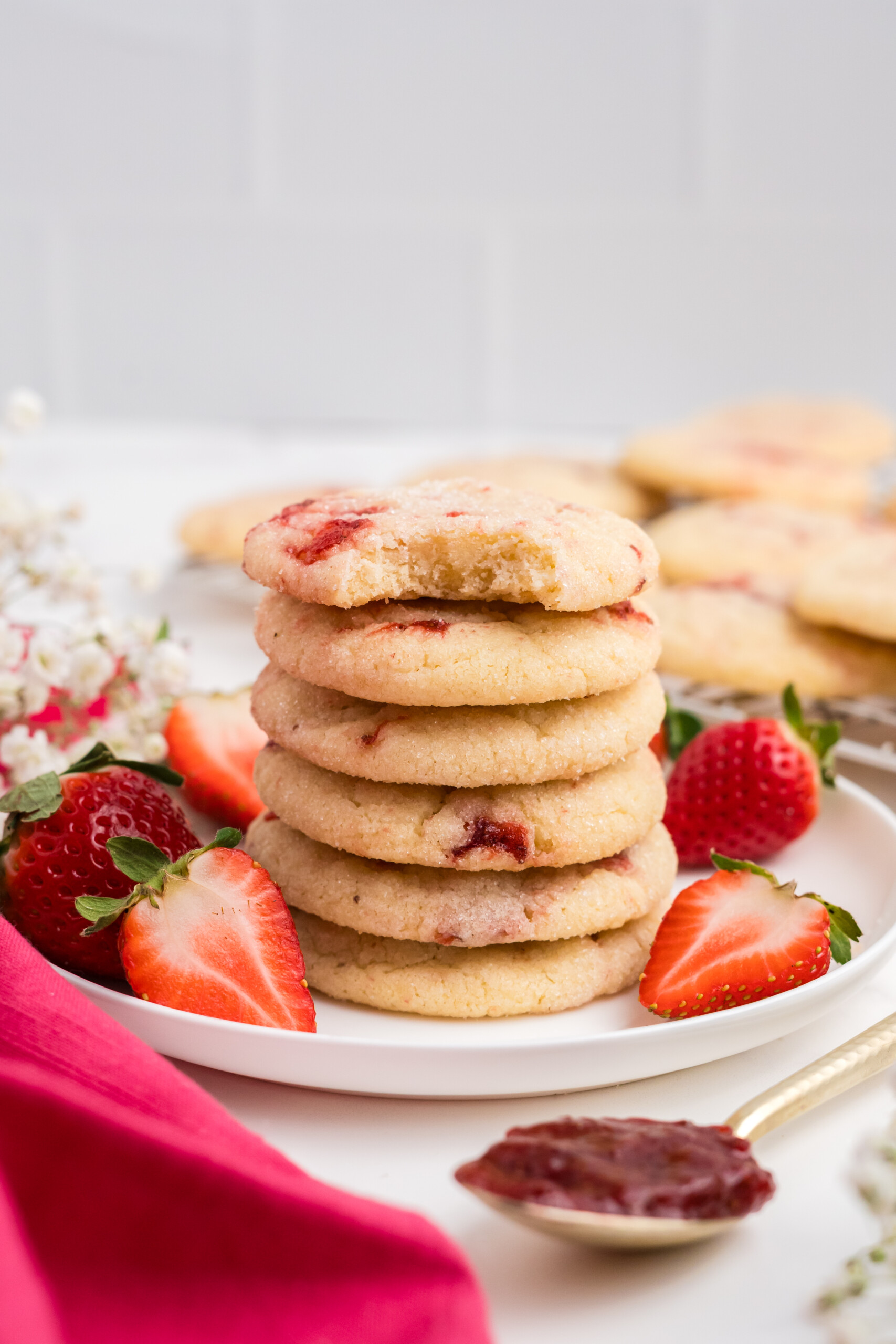 A stack of strawberry sugar cookies on a plate surrounded by strawberries.