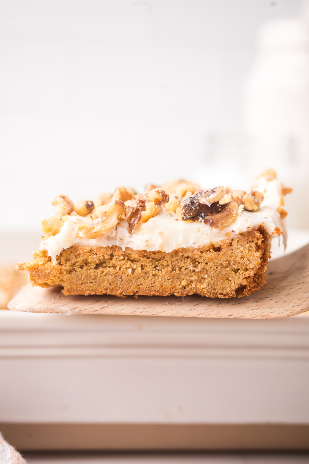 A spatula holding up a carrot blondie with frosting and walnuts on top.