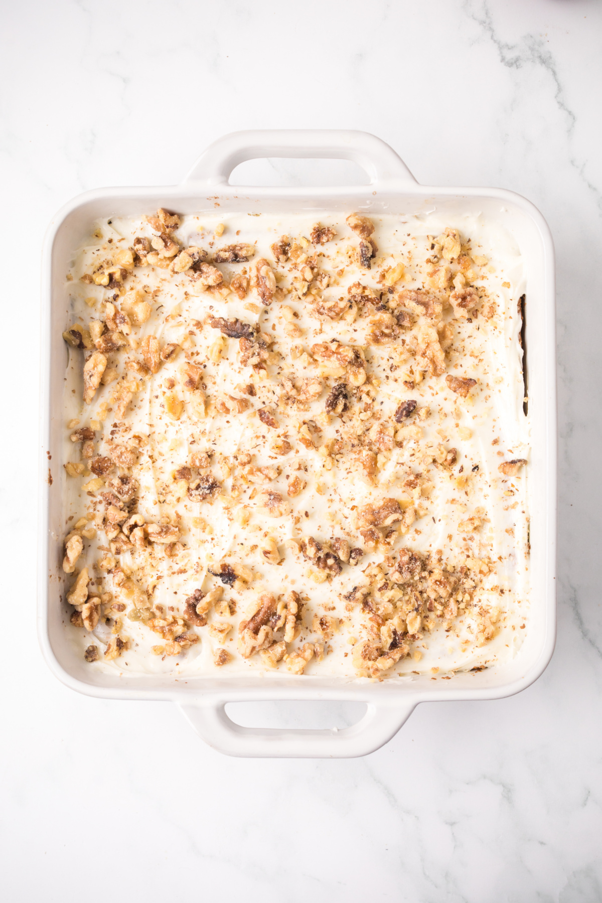 The blondie cooling and topped with frosting and a walnut garnish.