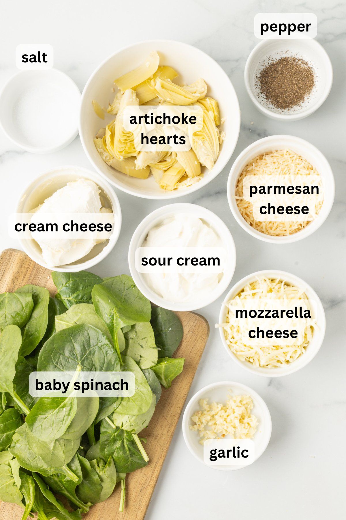 Ingredients to make this slow cooker spinach and artichoke dip in bowls on a table.