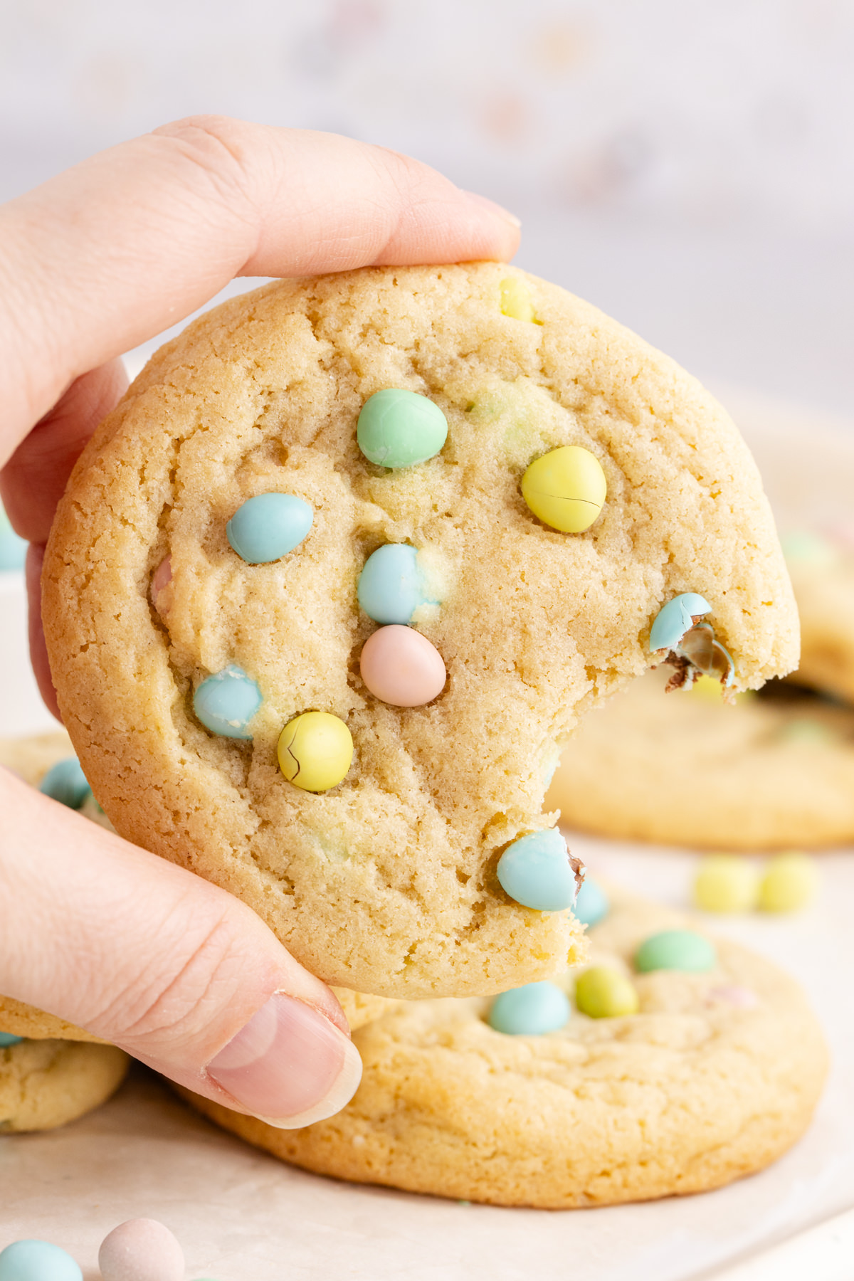 A cookie with chocolate eggs held up in the air with a bite taken out of it.
