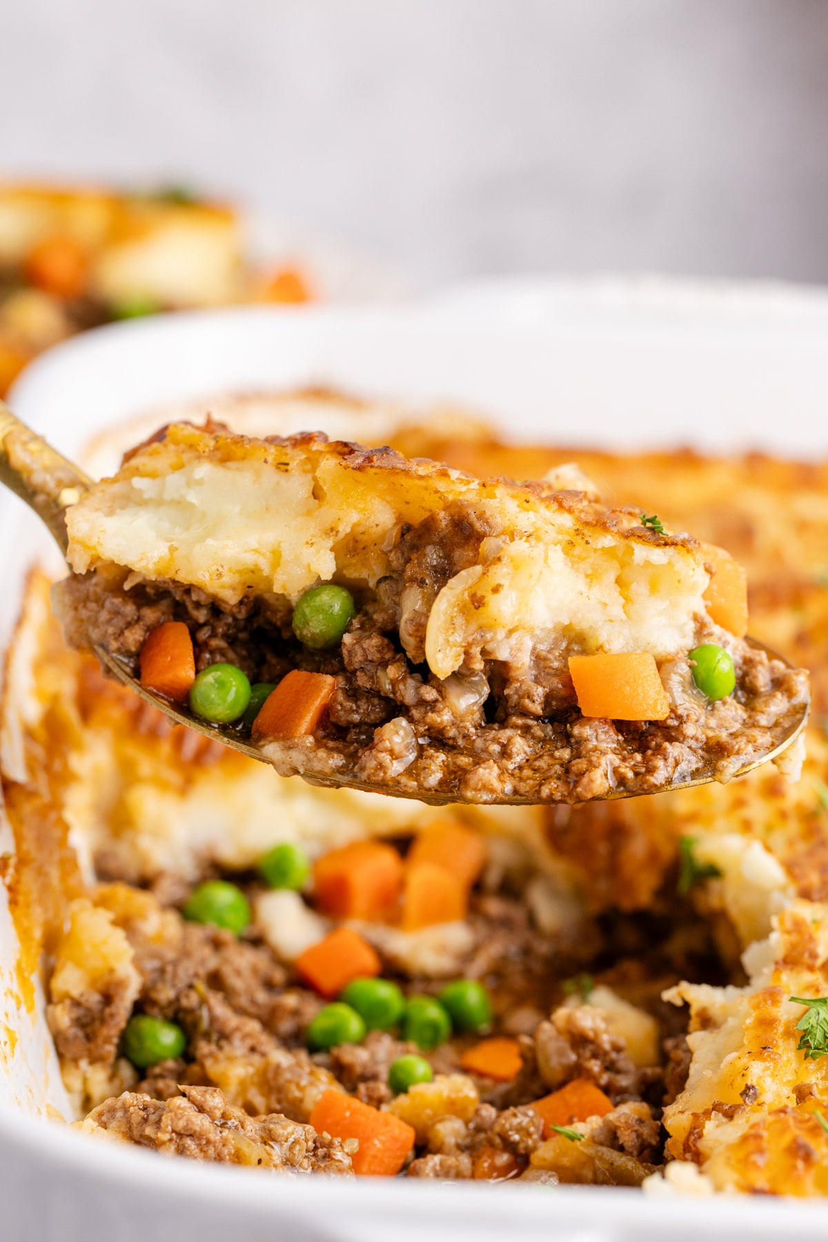 A spoon taking some cottage pie from the dish.