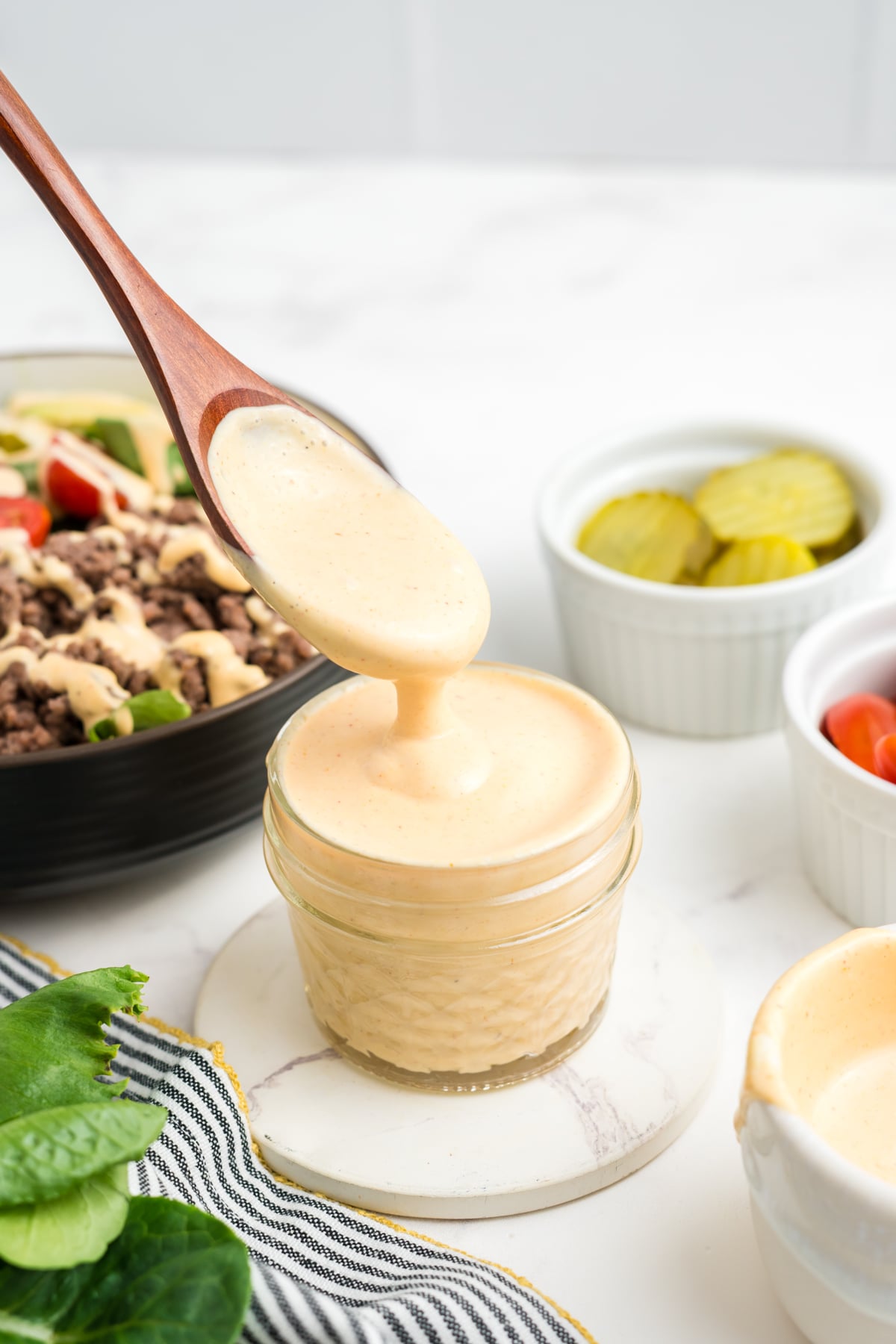 A jar of sauce with a spoon lifted out of sauce with sauce dripping back into the jar.