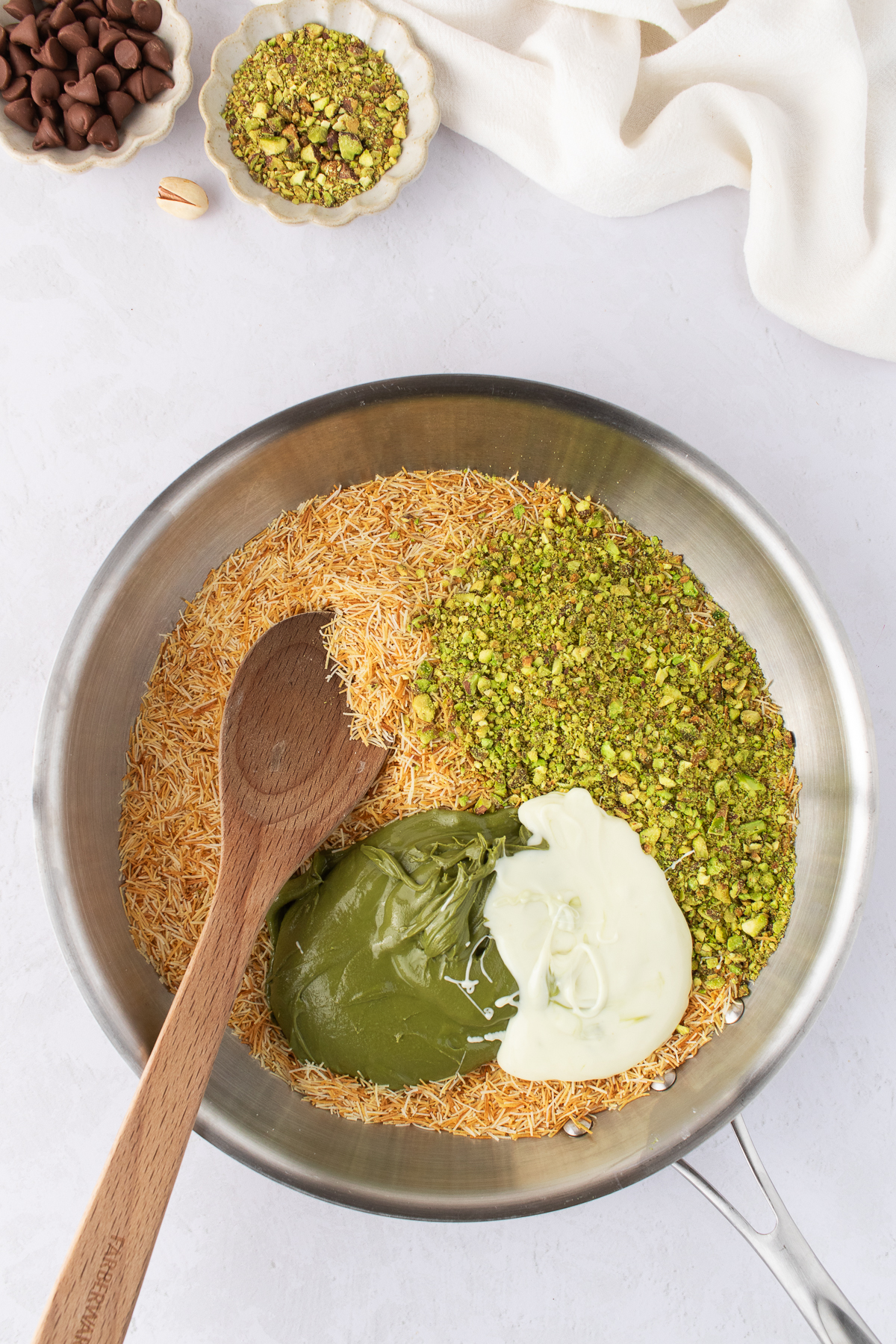 Toasted kataifi, white chocolate and pistachio cream in a skillet with a wooden spoon.