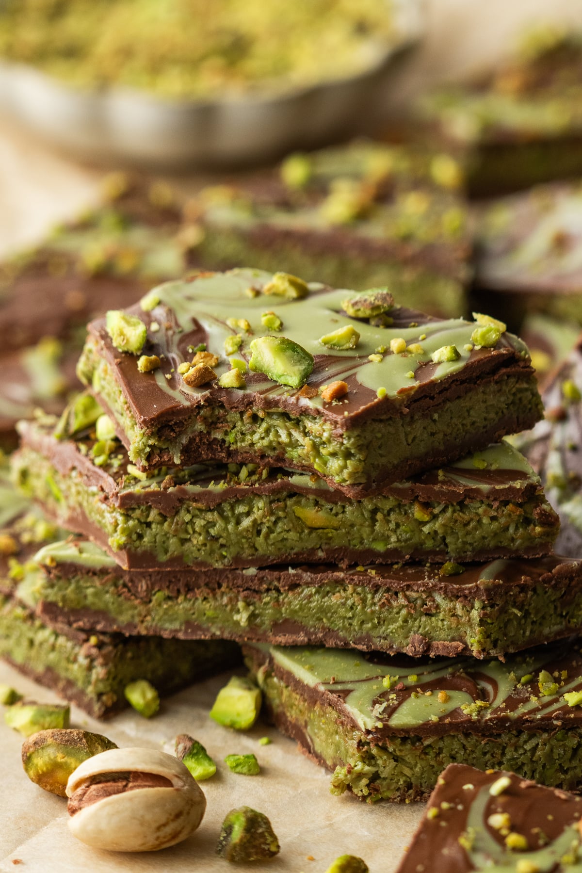 A stack of chocolate pistachio bark on parchment with pistachios and the top piece missing a bite.