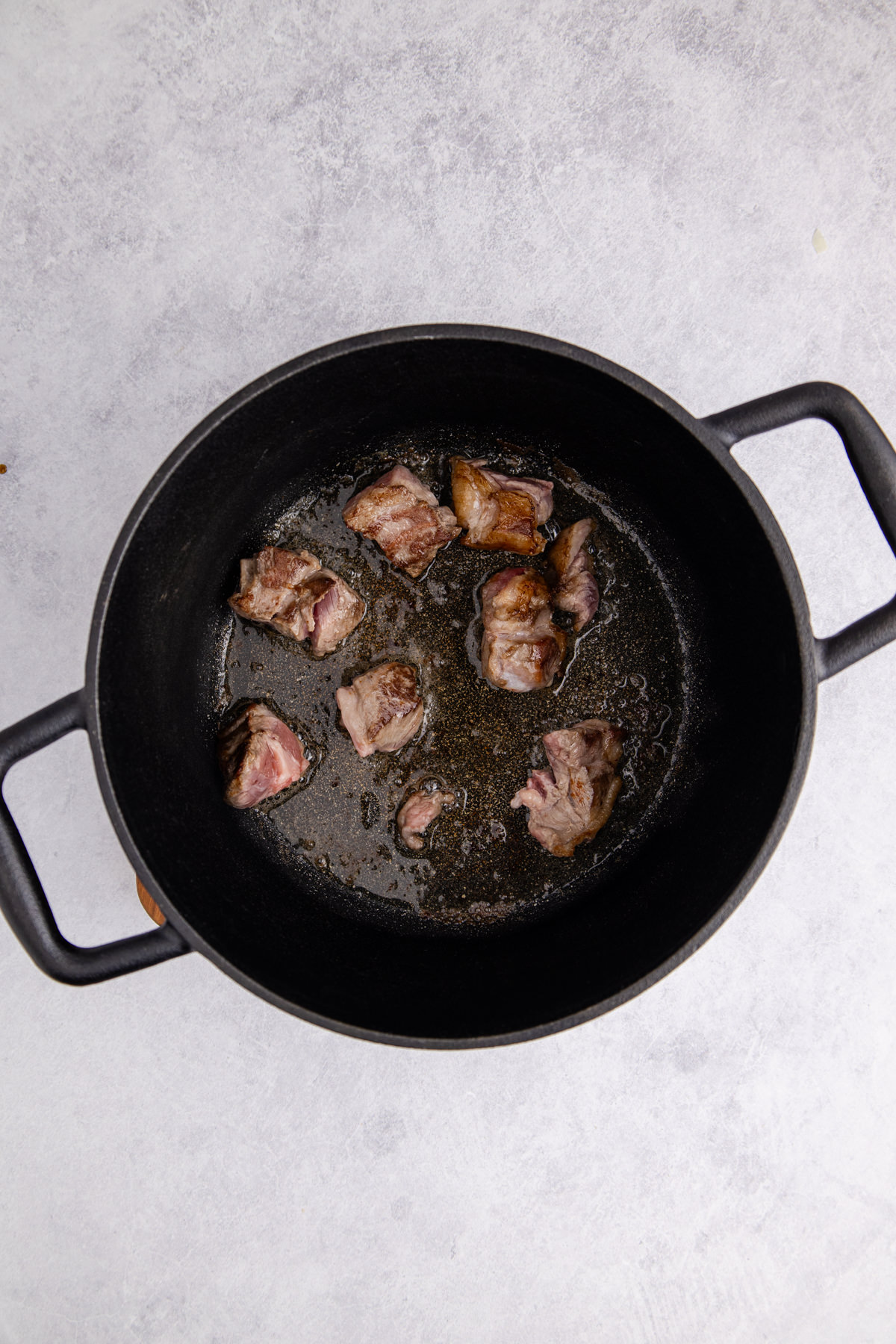 Pieces of lamb browning in a Dutch oven.