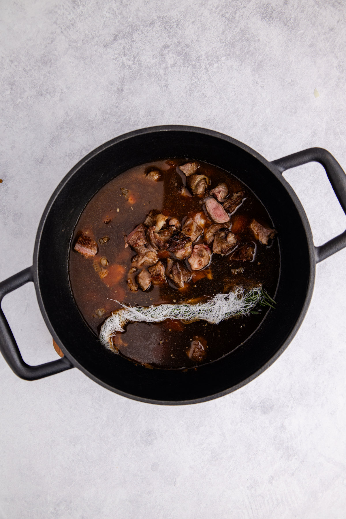 Lamb added to the dutch oven with rosemary, Worcestershire, and seasoning.