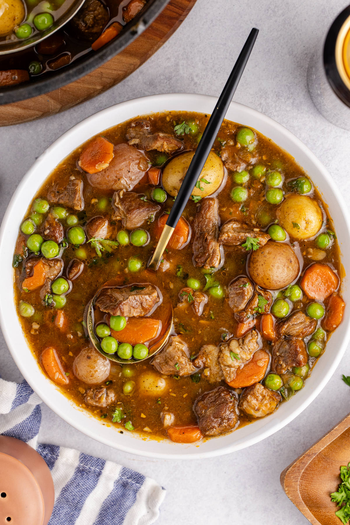 A bowl filled with lamb Irish stew and a ladle taking some out.