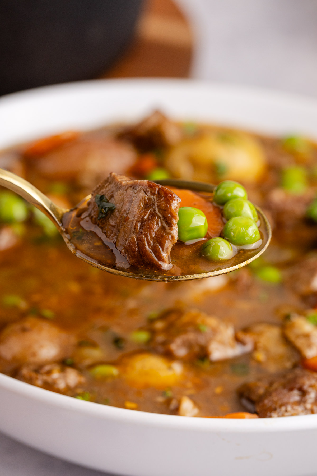 A spoon holding up some lamb, peas and carrots over a bowl of Irish stew.