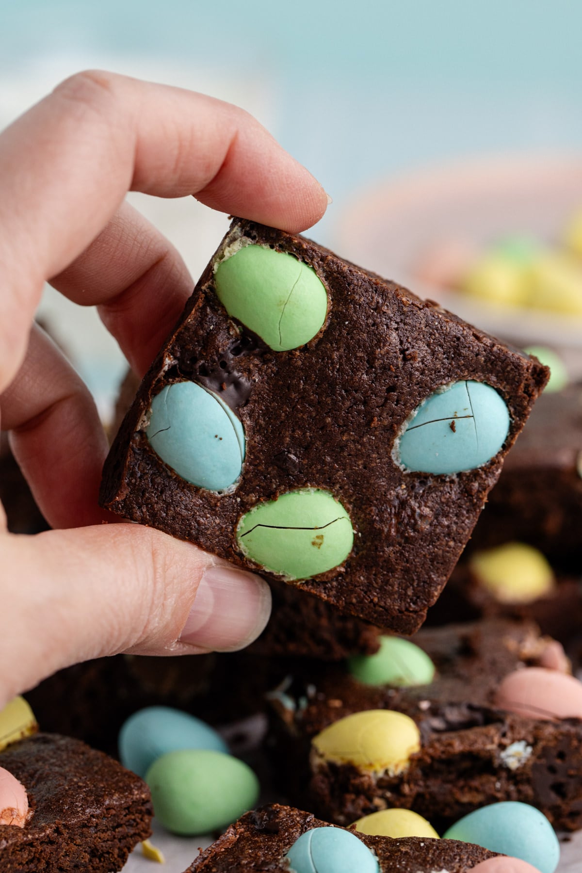 A hand holding up a brownie with Easter eggs in it.