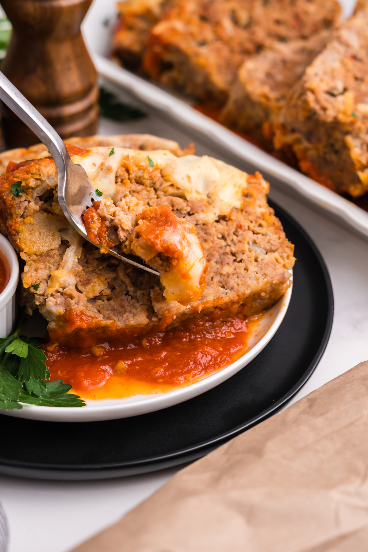 A fork holding a bite of Italian meatloaf over a plate of more. 