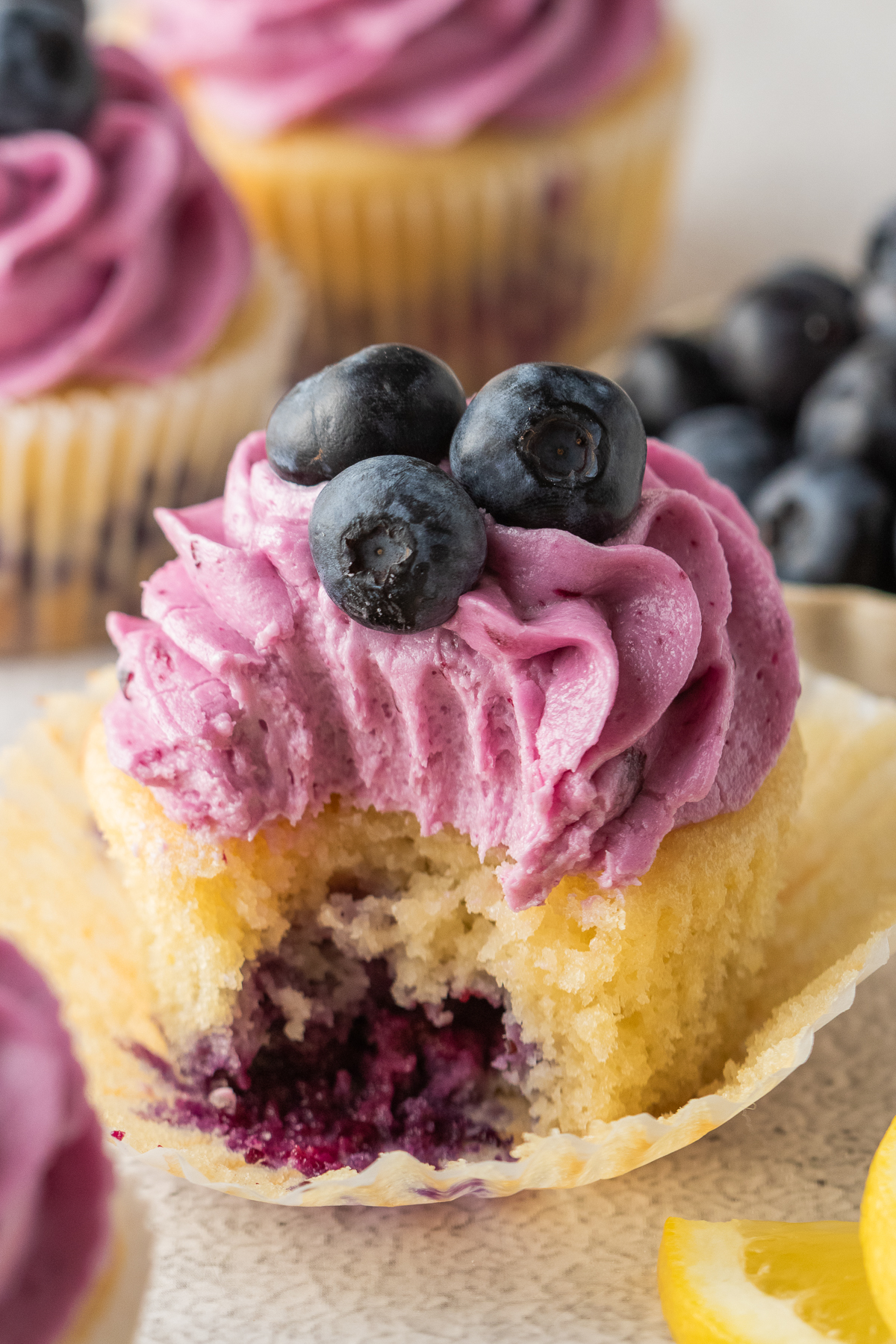 A lemon blueberry cupcake with a bite taken out of it on a table.