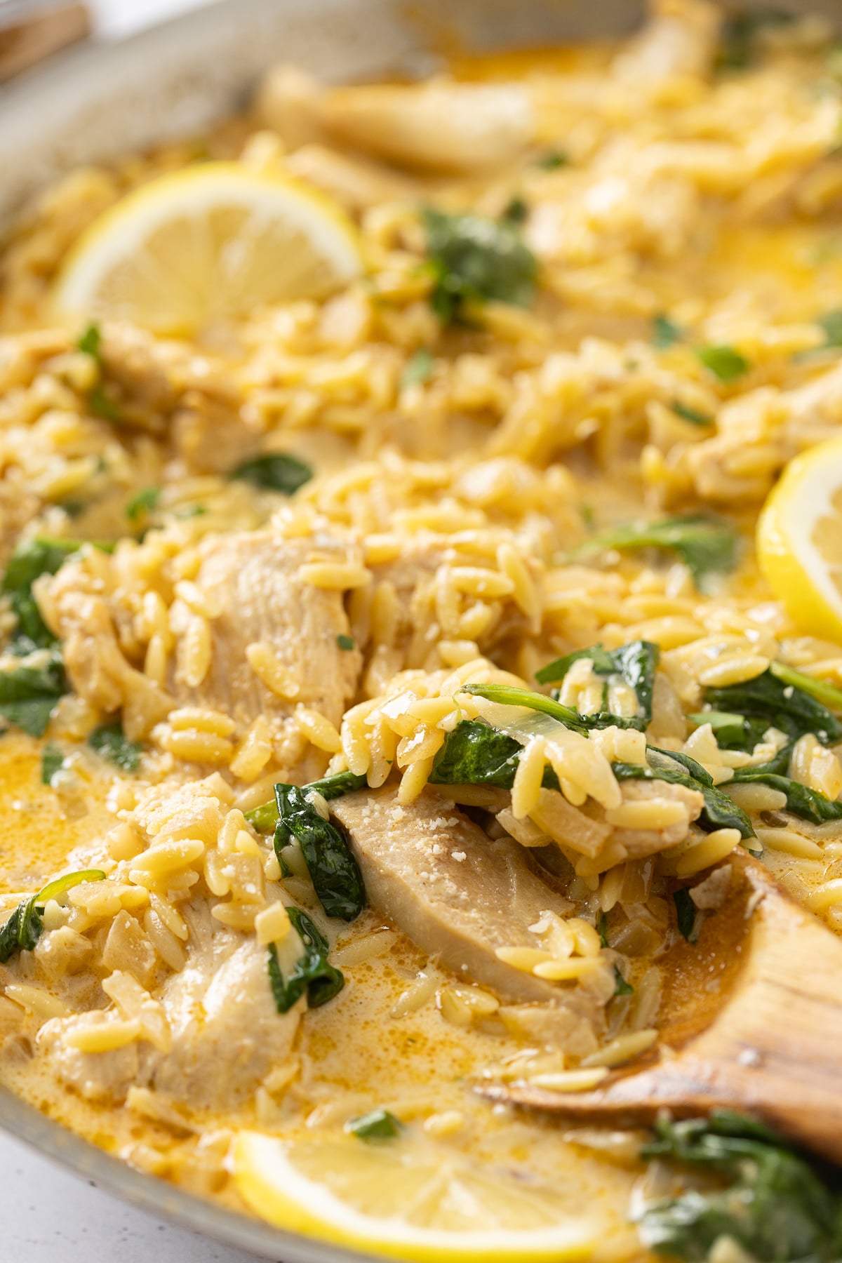 A wooden spoon mixing some lemon orzo with chicken.