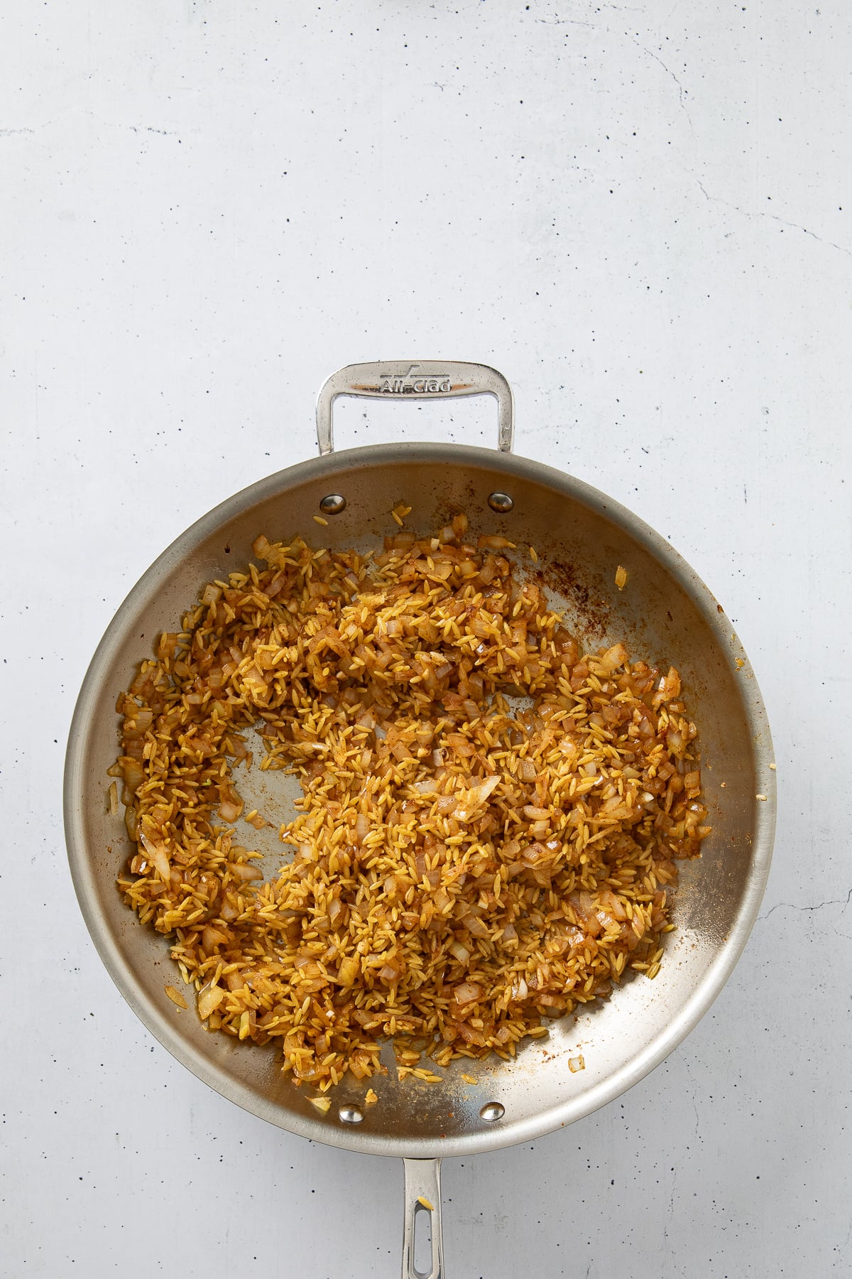 Onion, garlic and orzo saute cooking in a skillet.