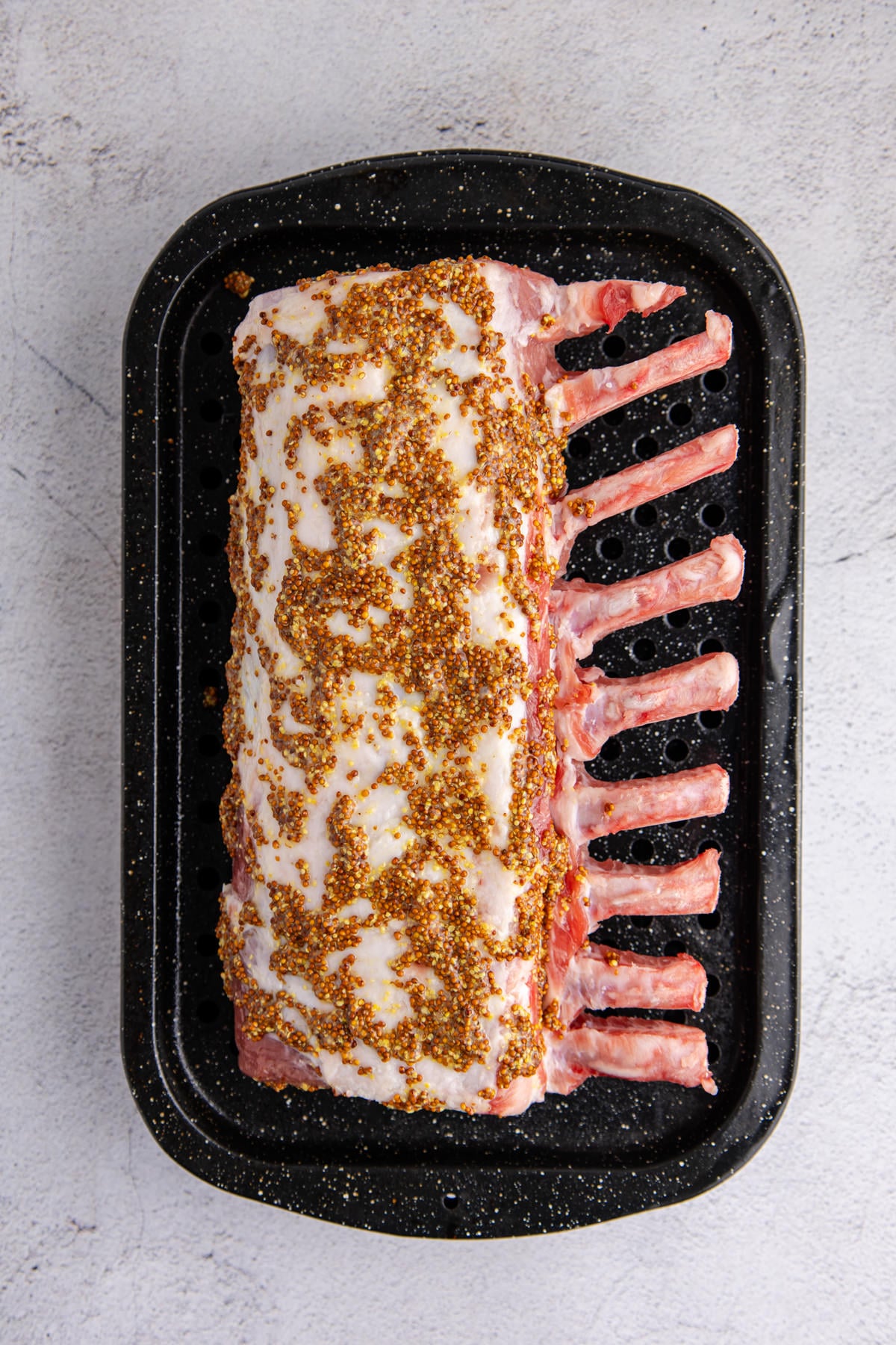 A pork prime rib on a roasting pan with grainy mustard and fresh thyme.