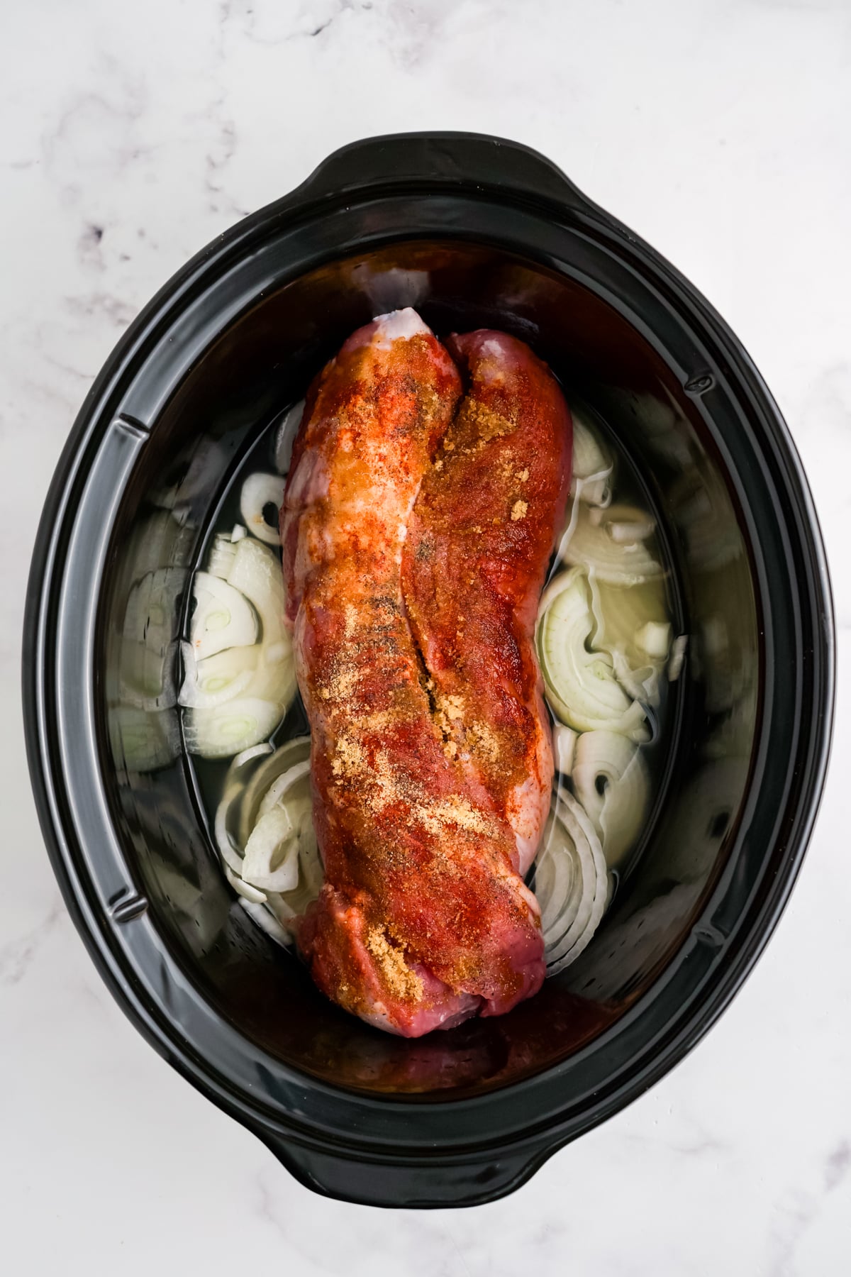Pork tenderloin over garlic and onions in a crock pot with a spice layer.
