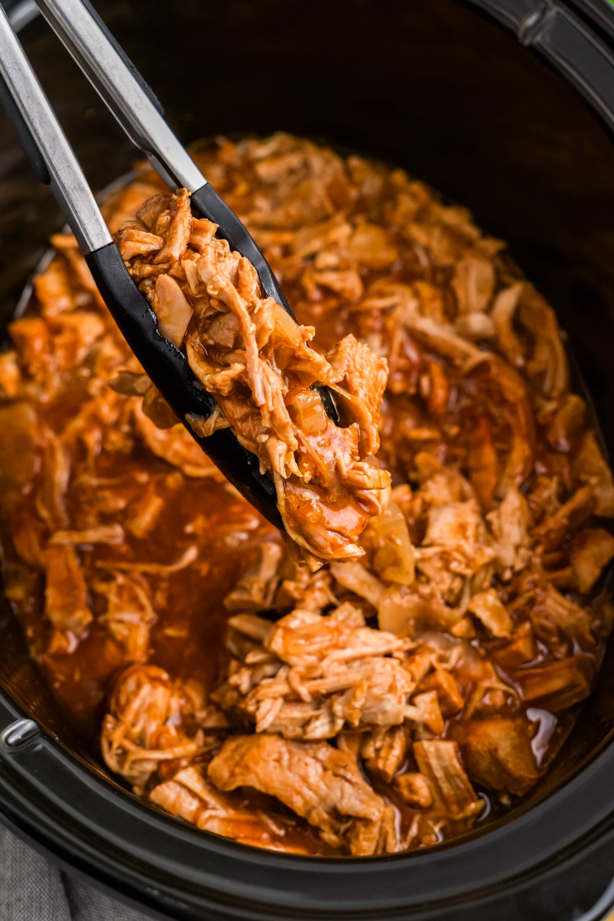 Shredded pork with BBQ sauce being picked up with tongs.