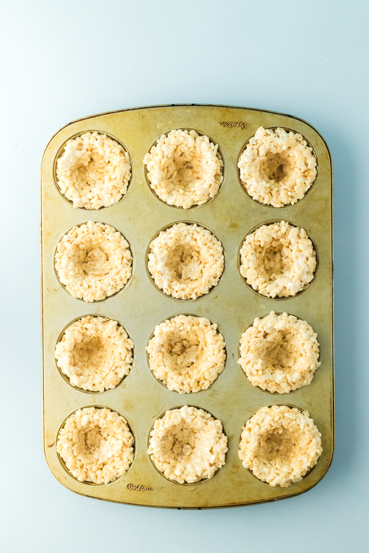 Twelve rice krispie nests lightly pressed into muffin pan.